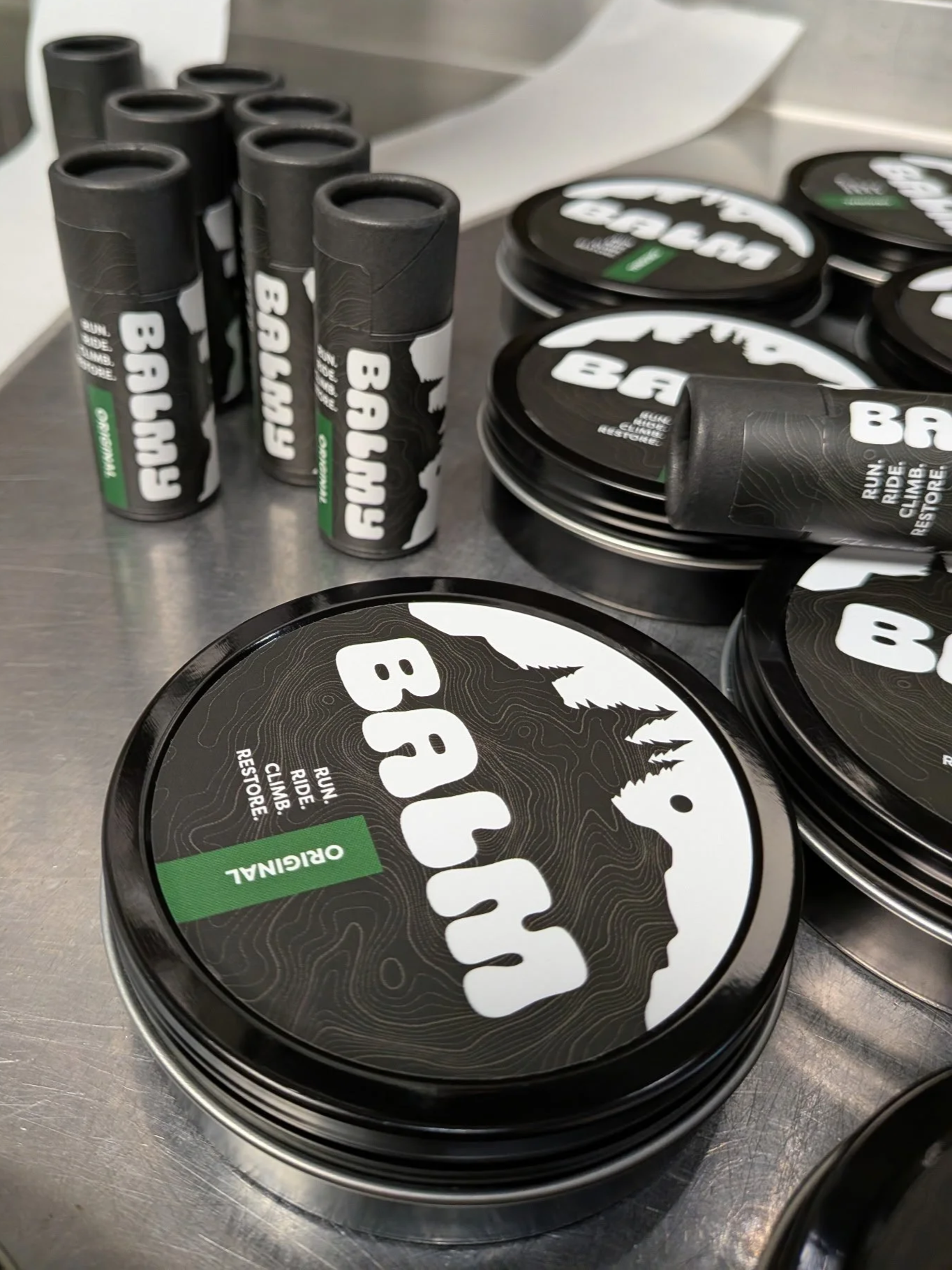 Container of BALM anti-chafe with a black lid and mountain logo, alongside BALMY sticks.