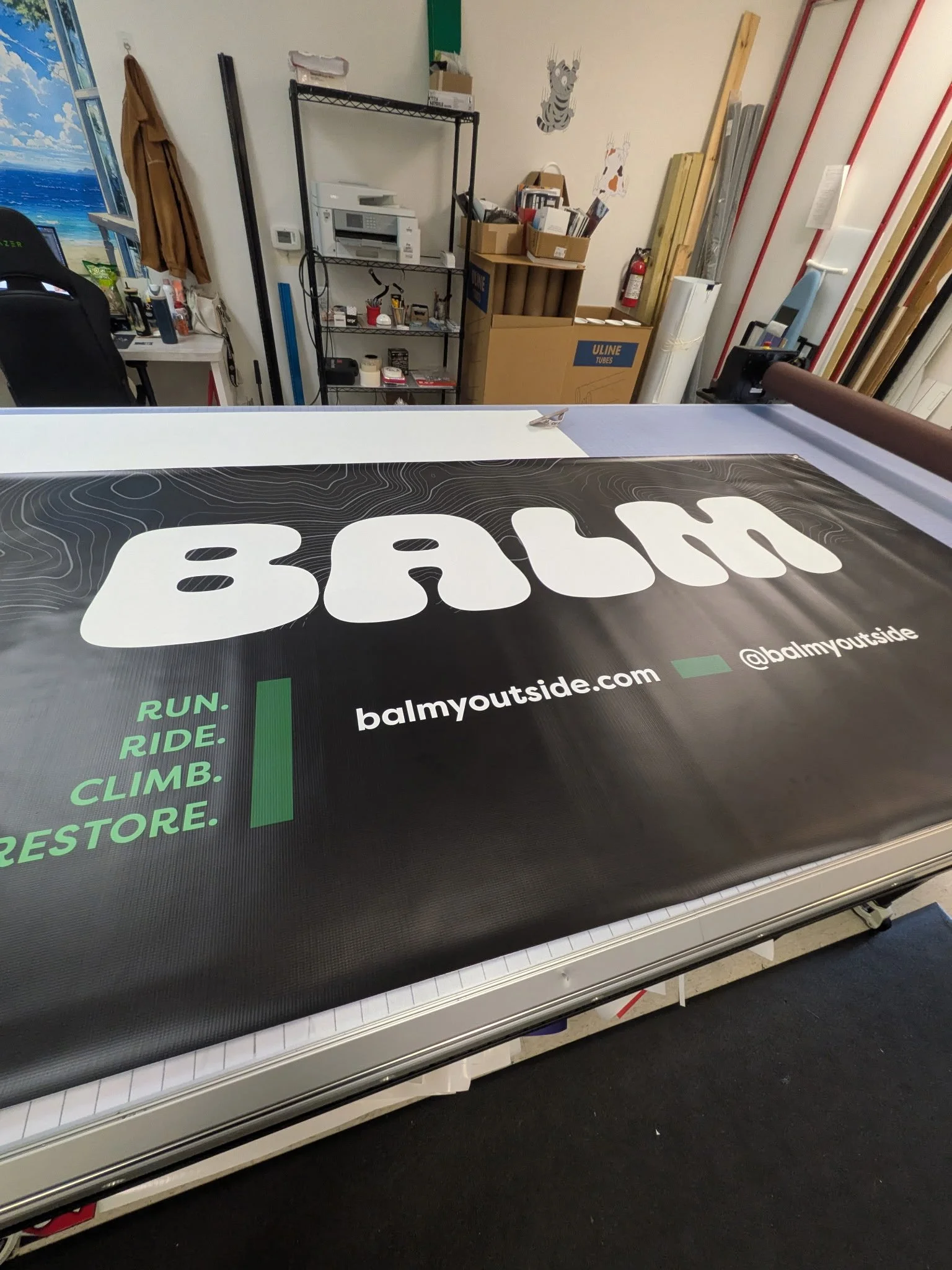 A close-up of a large black and white sign on a treadmill with the words 'BALMY' and the website address 'balmyoutside.com'.