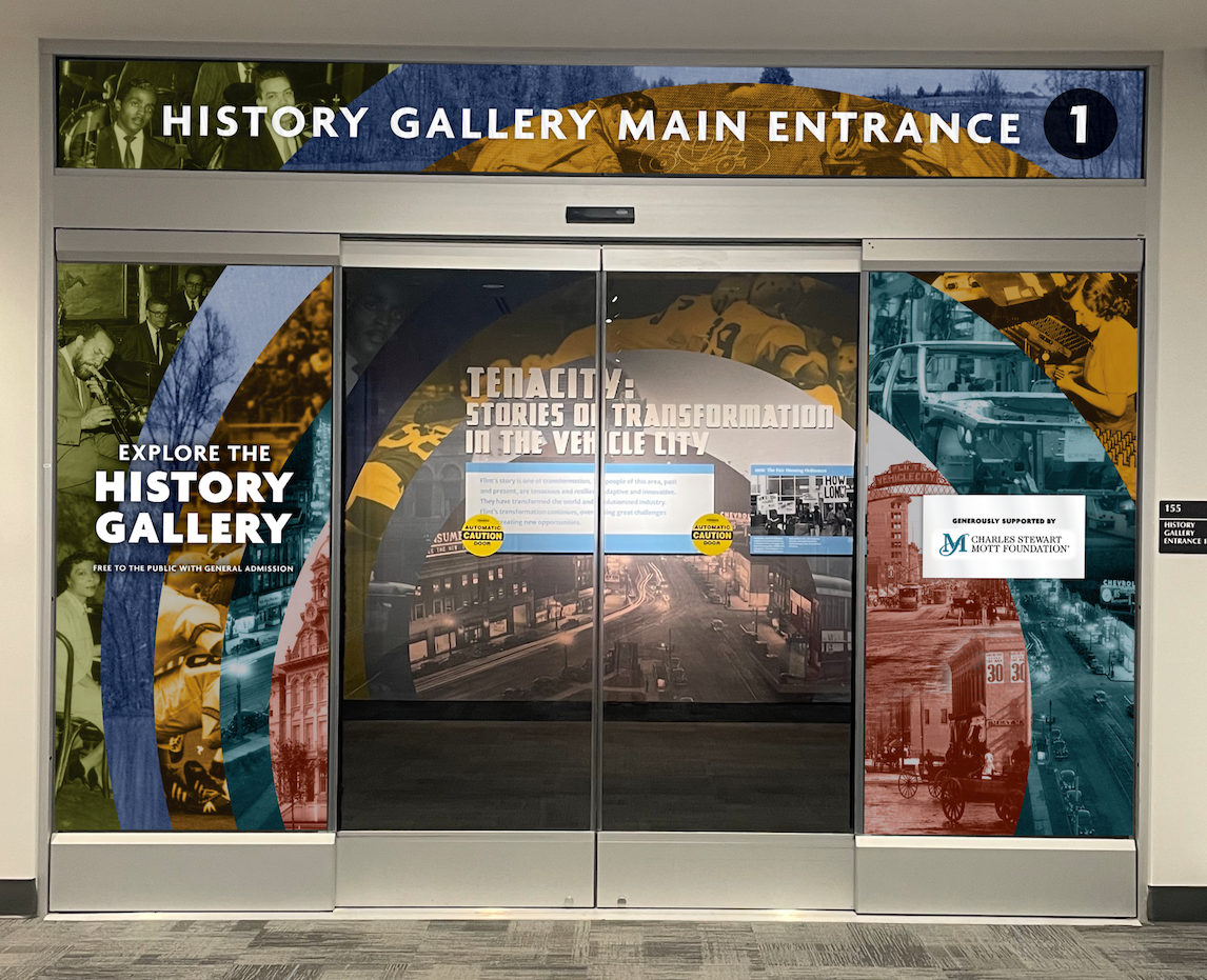 Entrance to the History Gallery with colorful graphic wraps and a sign that reads 'Tenacity: Stories of Transformation in the Vehicle City.'