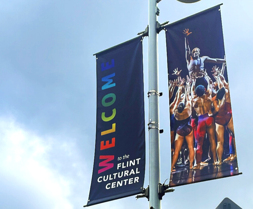 Banners at the FLINT Cultural Center, one says "Welcome" in colorful letters, and the other shows people in dance or performance costumes.