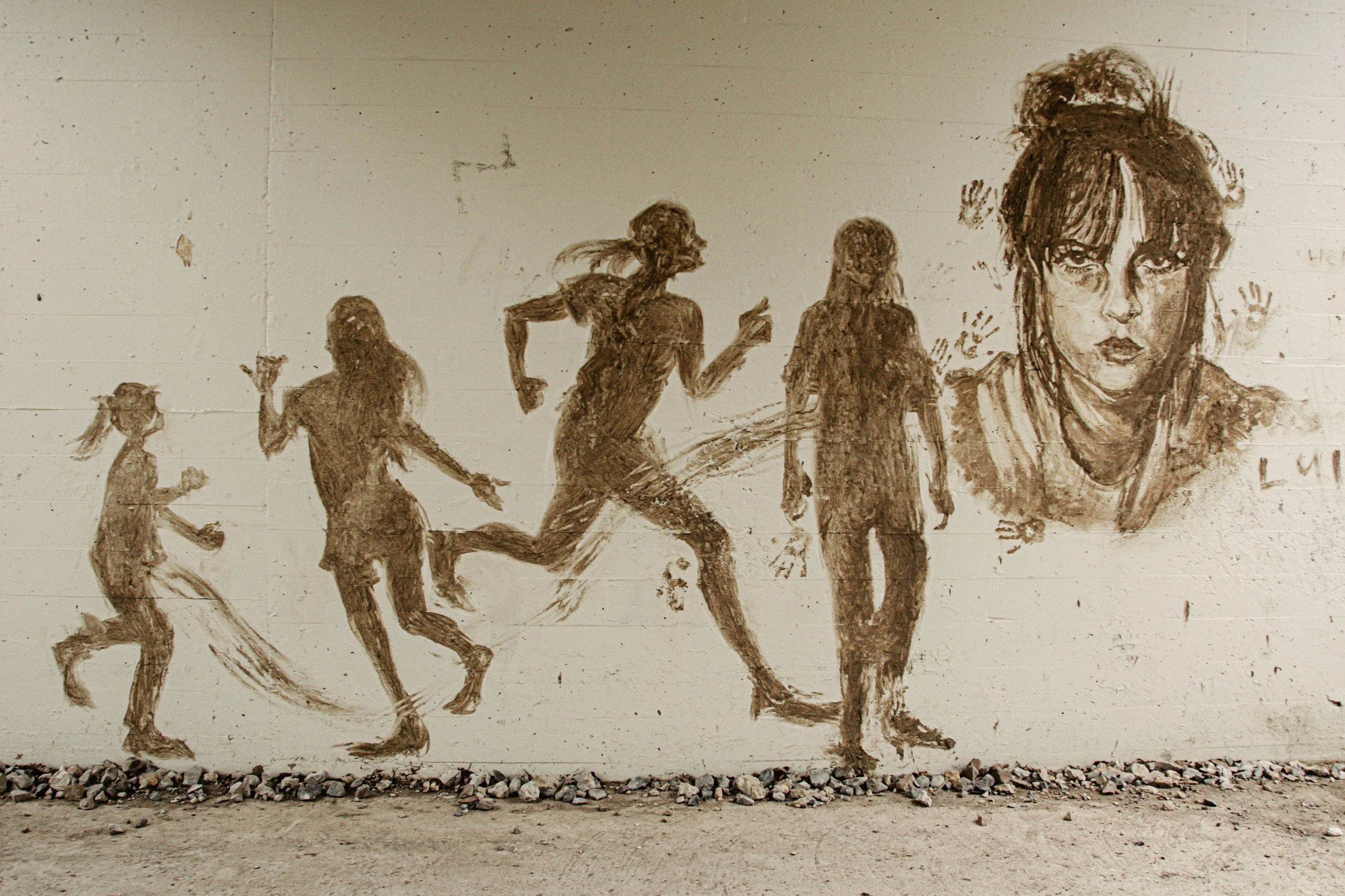 Murals of five young girls and one woman, depicted in various stages of running, painted in sepia tones on a white brick wall. The largest portrait features a woman with messy hair and intense eyes.