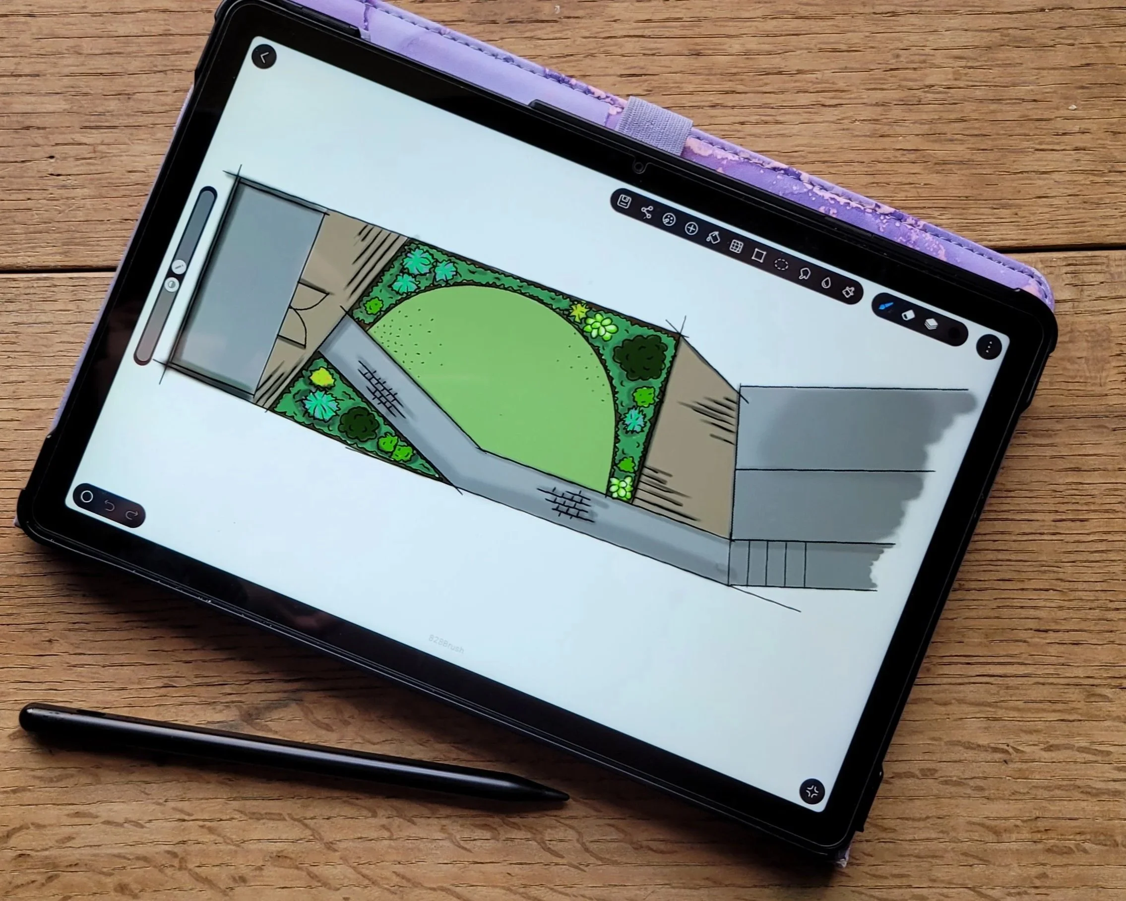 Digital illustration of a backyard garden with a lawn, pathway, and surrounding plants, displayed on a tablet with a stylus resting nearby on a wooden surface.
