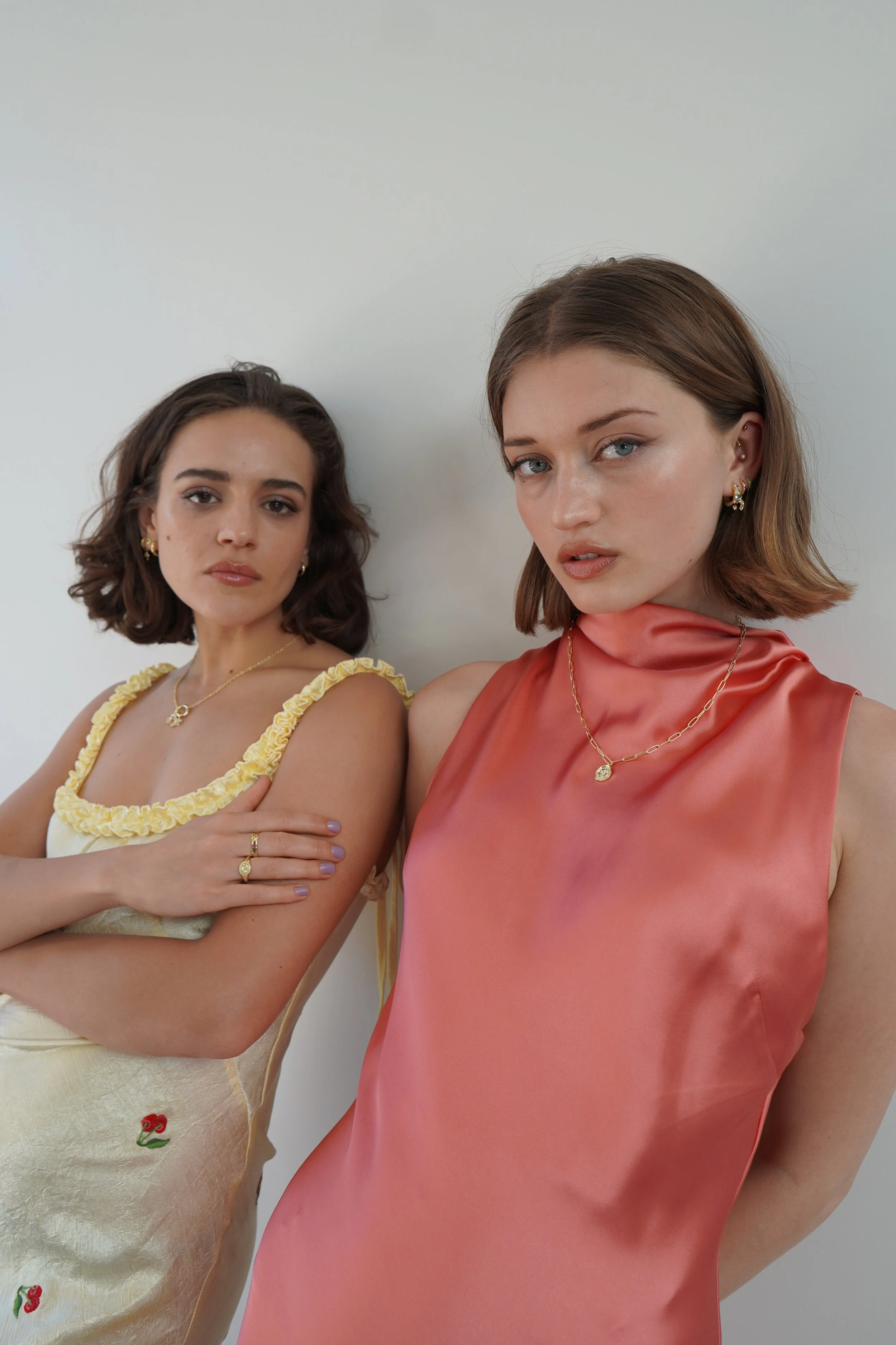 Two women with short brown hair and jewelry posing against a plain white wall.