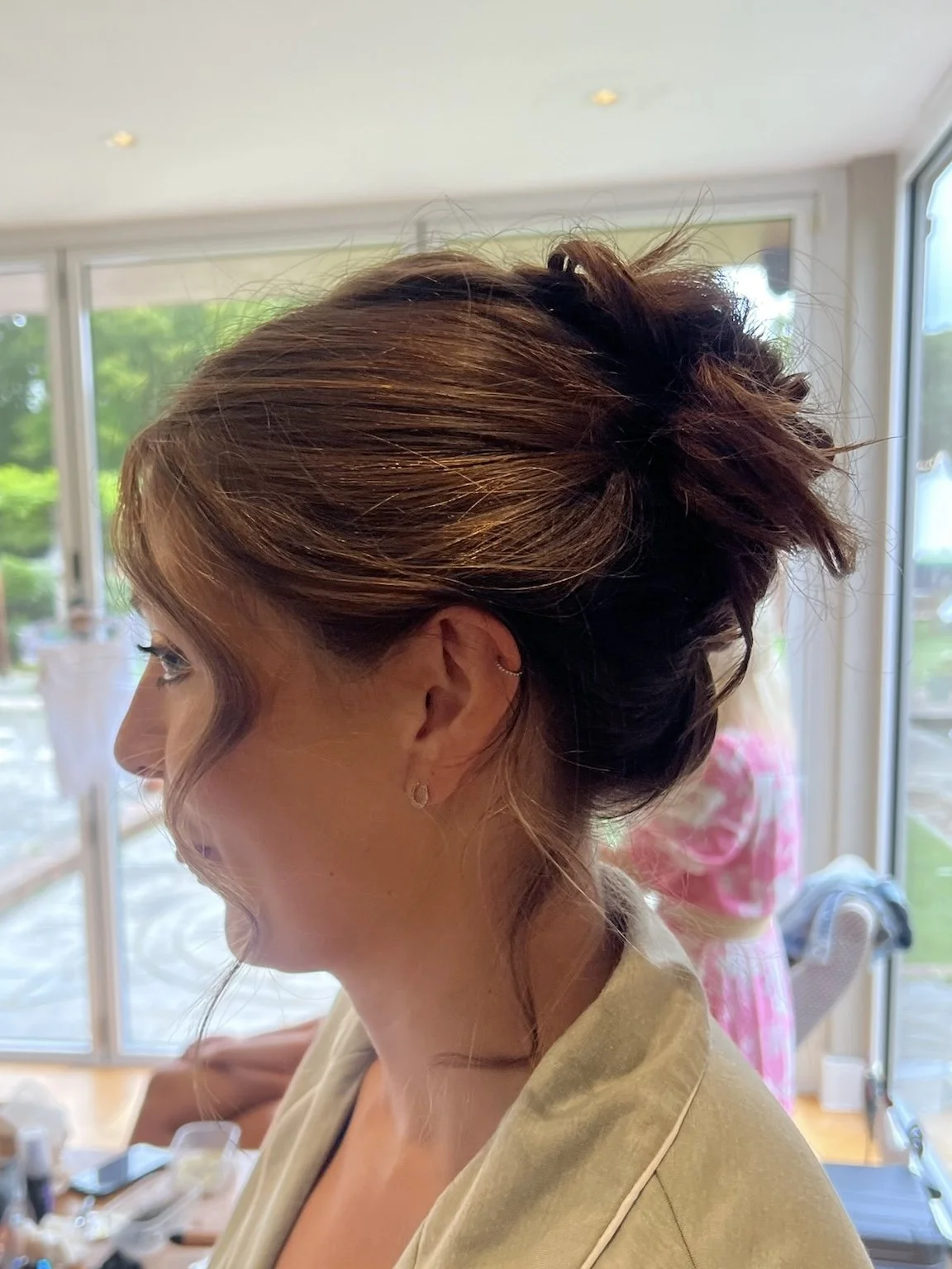 Woman with styled hair in an updo, side view, indoors near large windows.