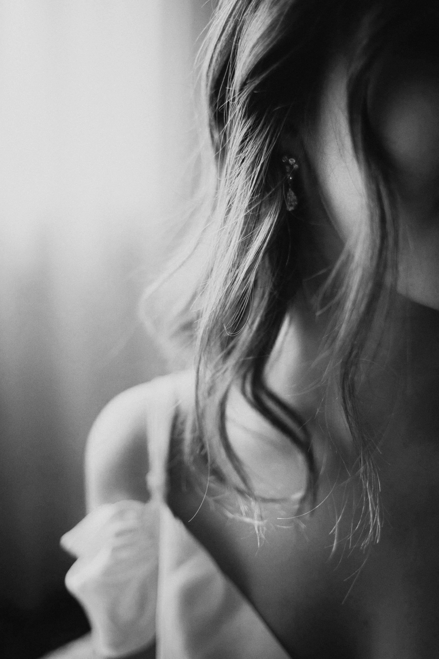 Close-up black and white photo of a woman's face partially visible, focusing on her curly hair and earrings.
