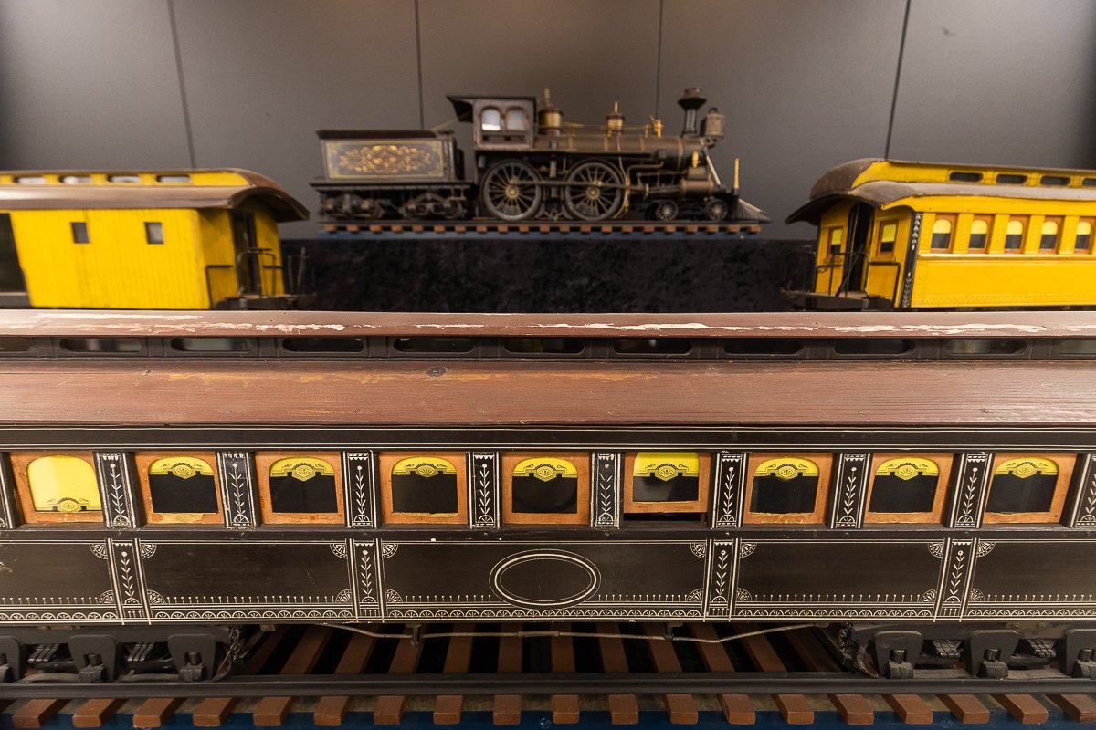 Model train with a black locomotive, yellow passenger cars, and a black and gold caboose on a track.