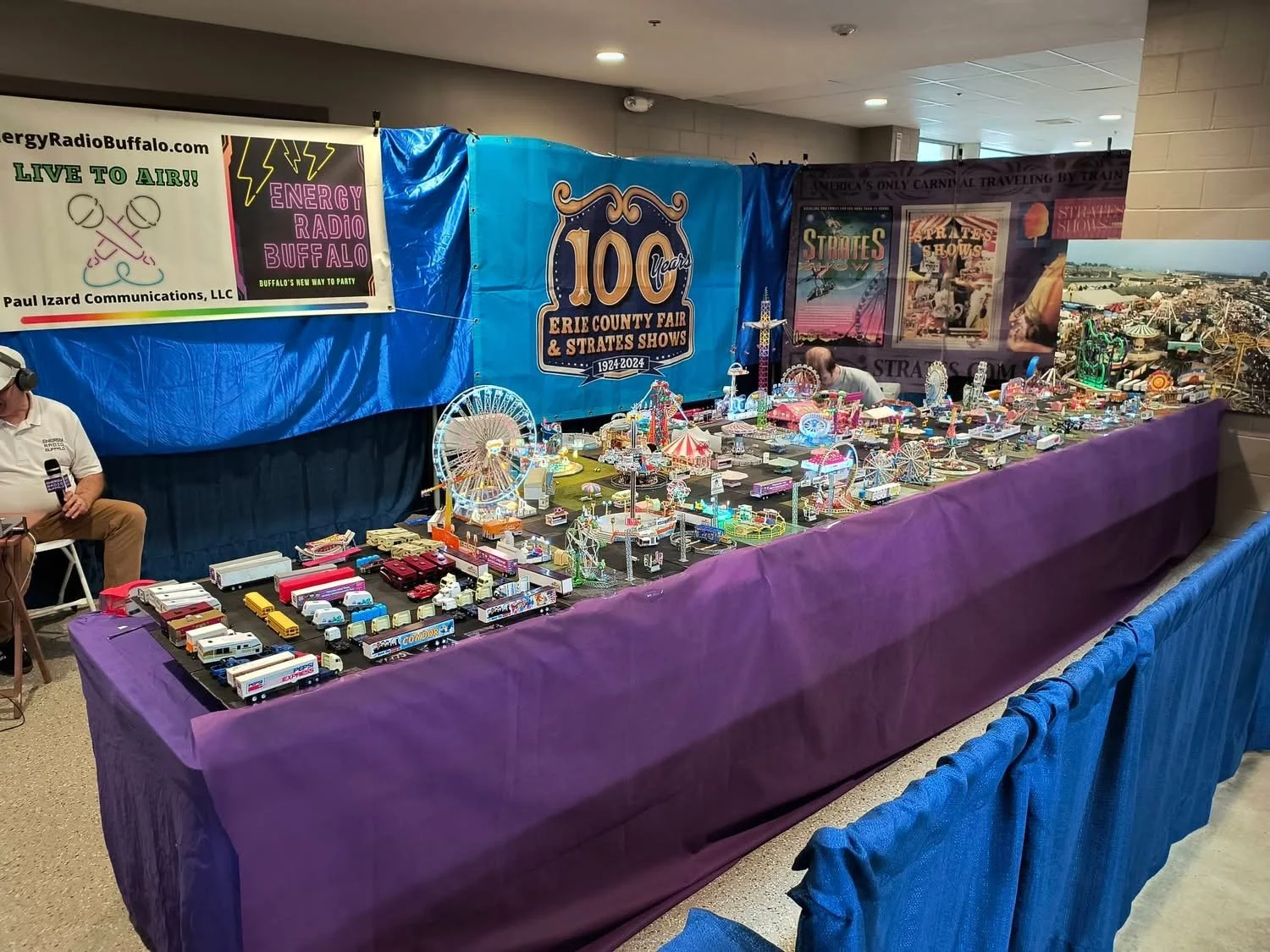 Display table featuring miniature carnival rides and vehicles at the Erie County Fair and Strates Shows exhibition, with banners celebrating the 100th anniversary of the Erie County Fair.