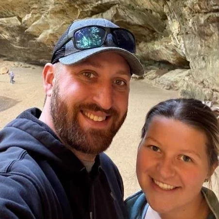 A man and a young girl smiling for a selfie in a rocky outdoor setting.