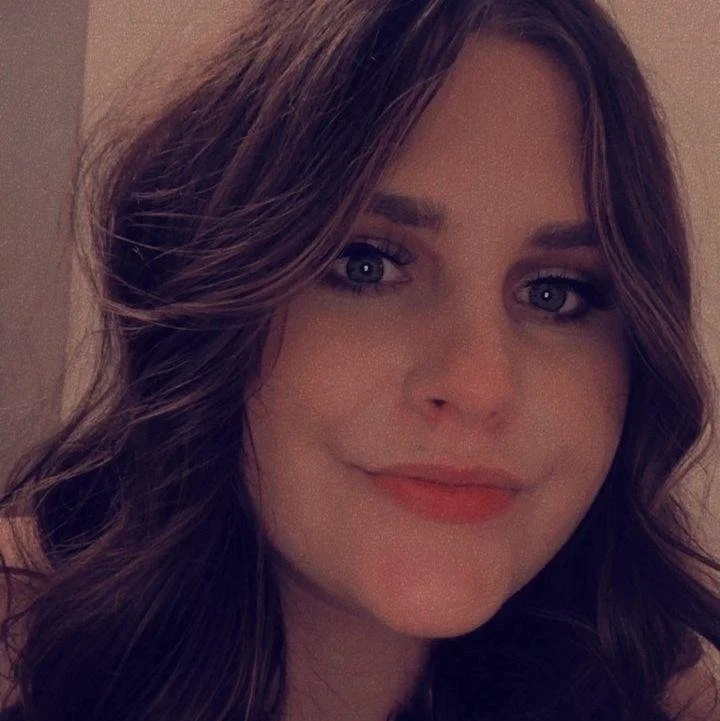 Close-up of a young woman with wavy brown hair and blue eyes, smiling softly.