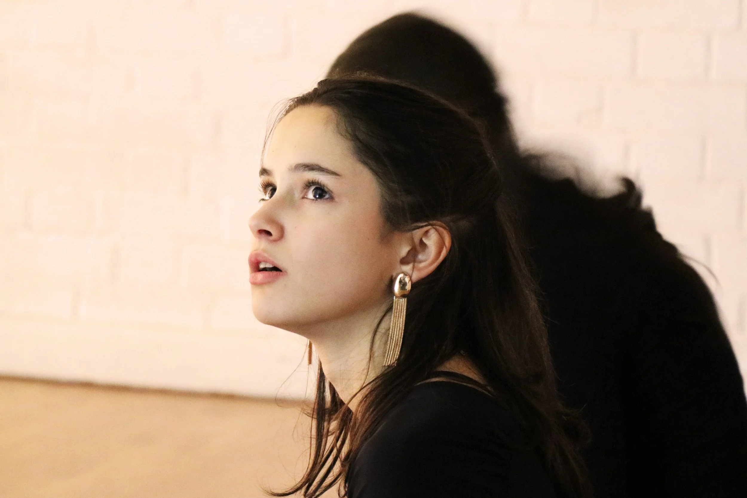 Close-up profile of a young woman with dark hair and earrings, looking to the left, with a blurred background.