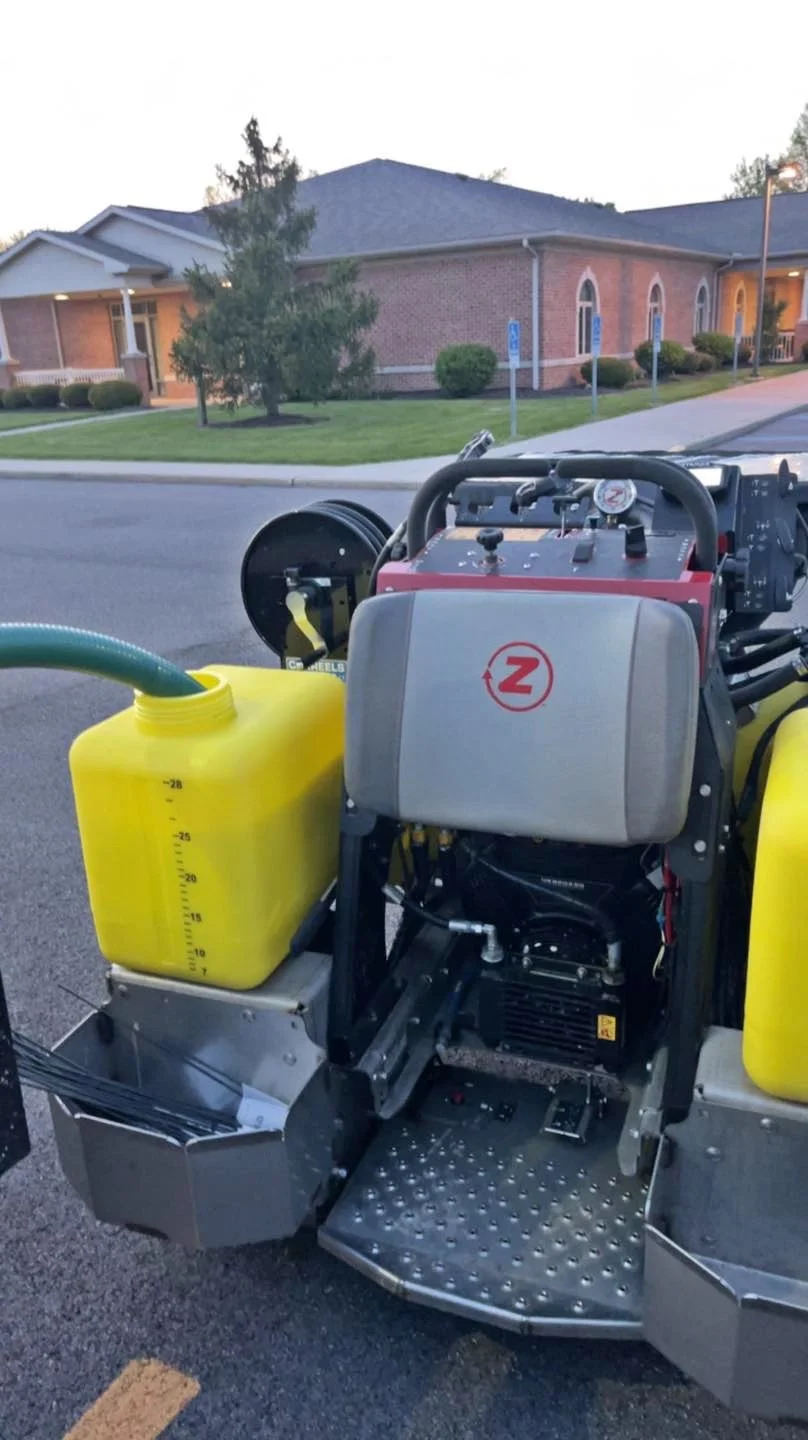 A sewer inspection robot with yellow tanks and control panels is parked on the street in front of residential houses.