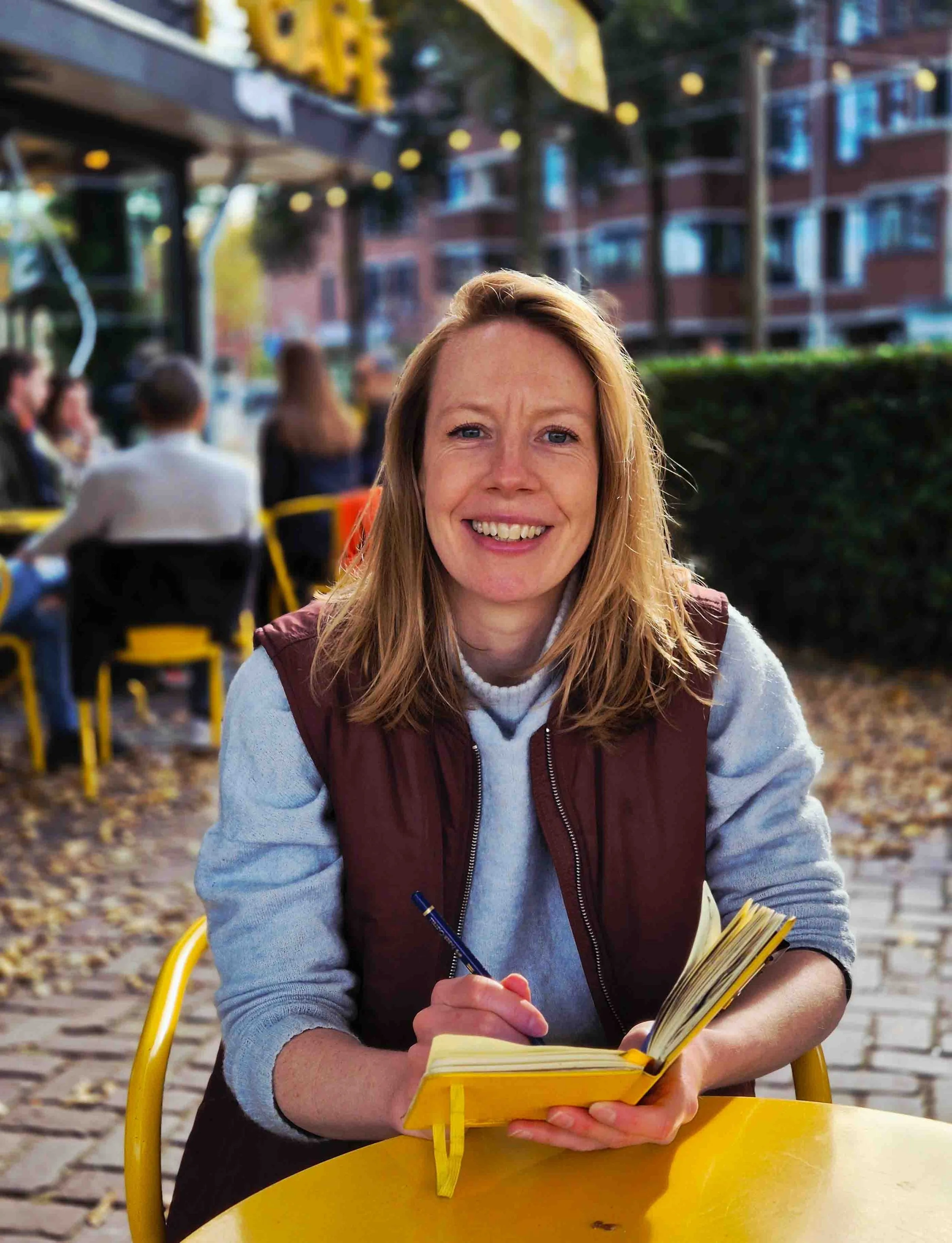 Ellie is sat with a pencil and sketchbook in hand, looking at the camera