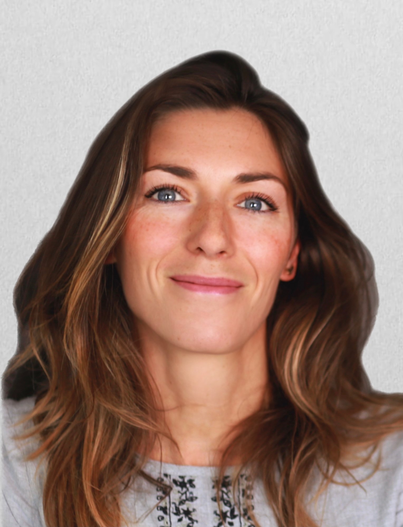 Une femme souriante avec de longs cheveux bruns, yeux bleus et une peau claire, portant un t-shirt gris à motifs noirs.