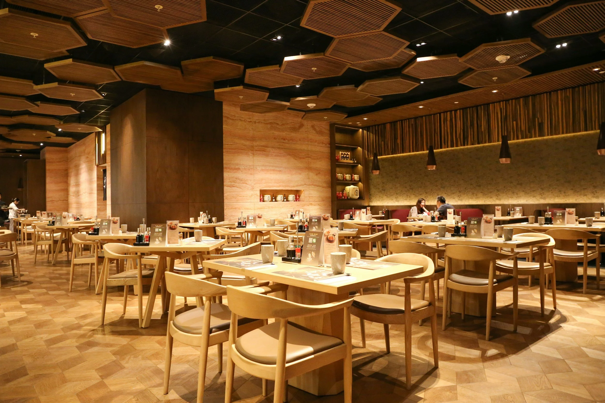 Interior of a modern restaurant with wooden tables, chairs, and a warm ambiance.