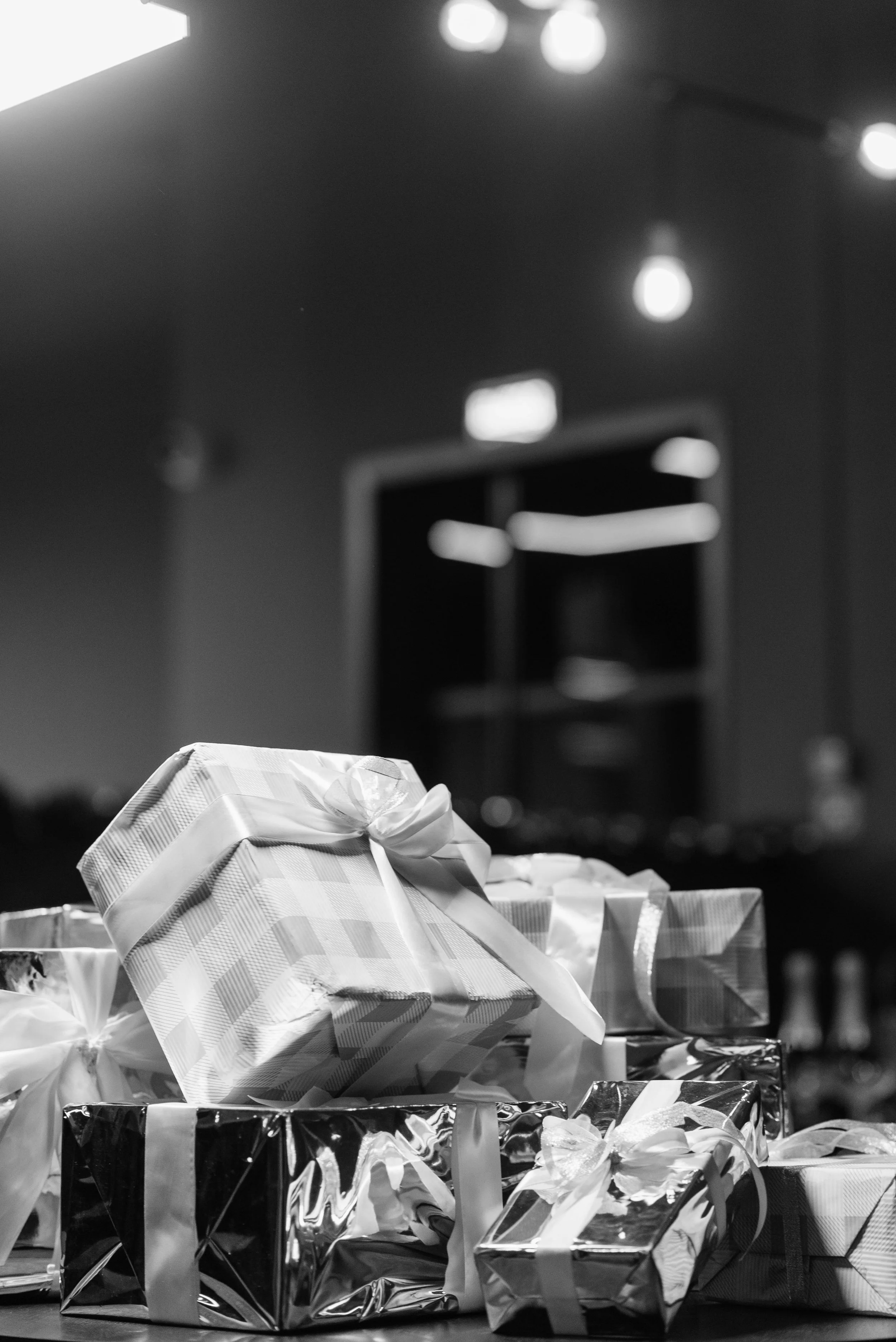 Stacked wrapped presents with ribbons in a dimly lit room.
