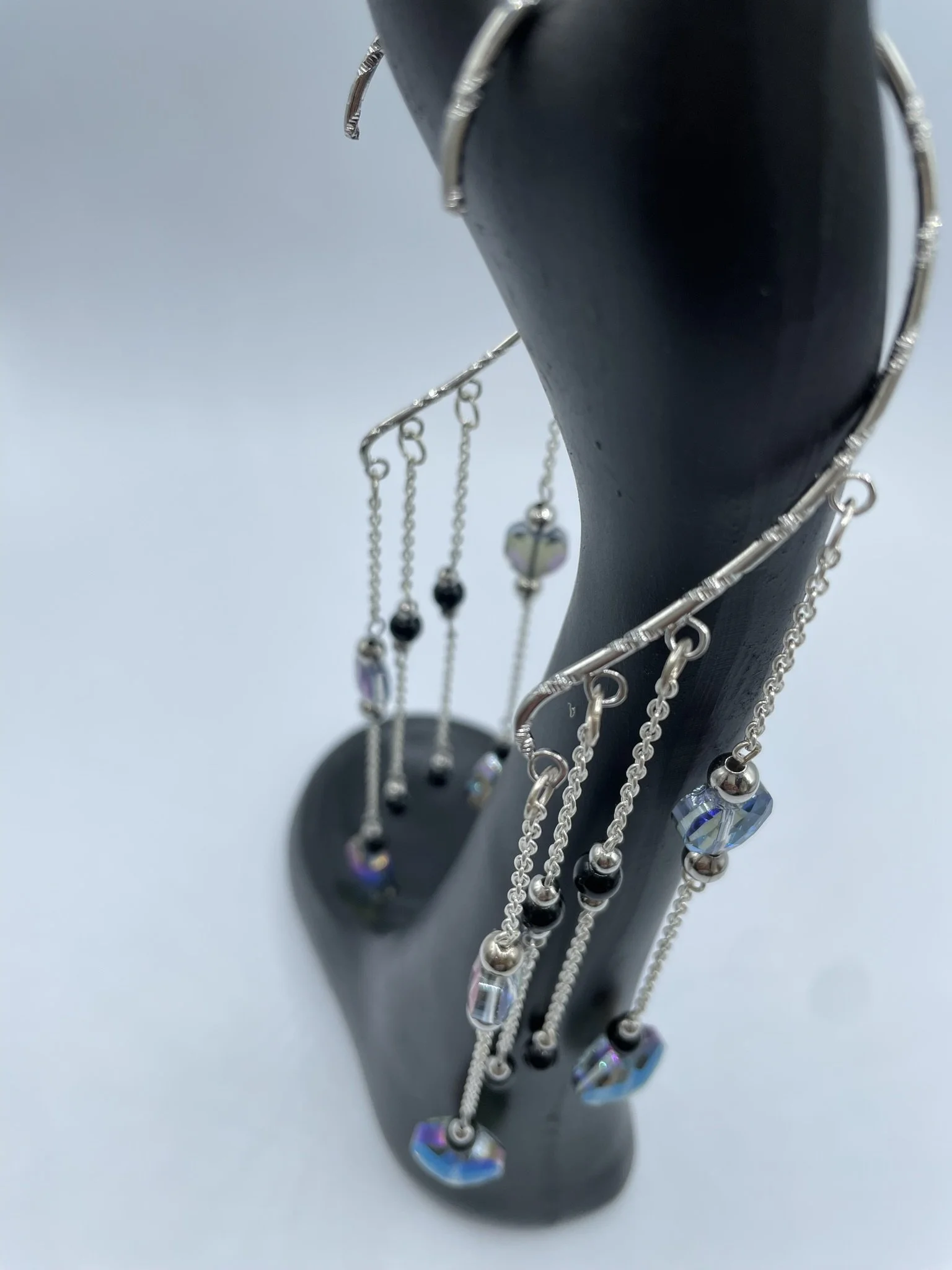 A black jewelry display stand with several silver dangling earrings featuring small black and iridescent beads.