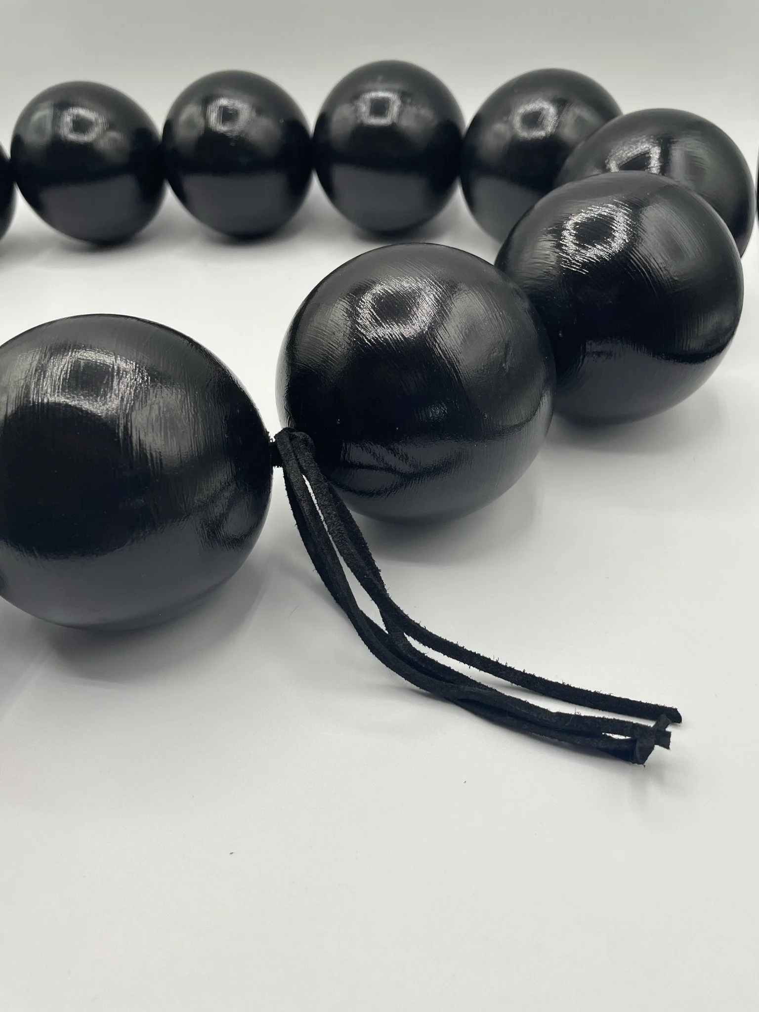 Close-up of black wooden beads strung together, with a few beads in focus and the rest blurred in the background on a white surface.