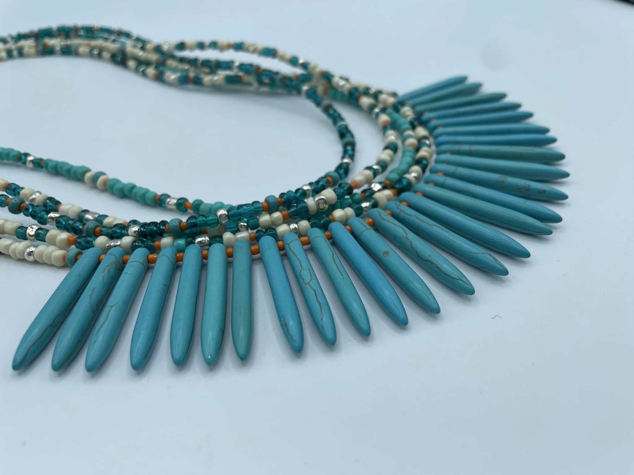 A turquoise beaded statement necklace with elongated teardrop-shaped pendants against a plain background.