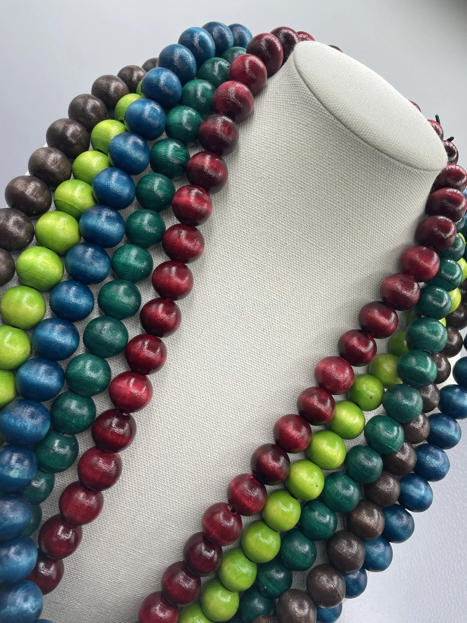 Colorful wooden bead necklaces in red, blue, green, brown, and teal, draped over a white fabric mannequin bust.