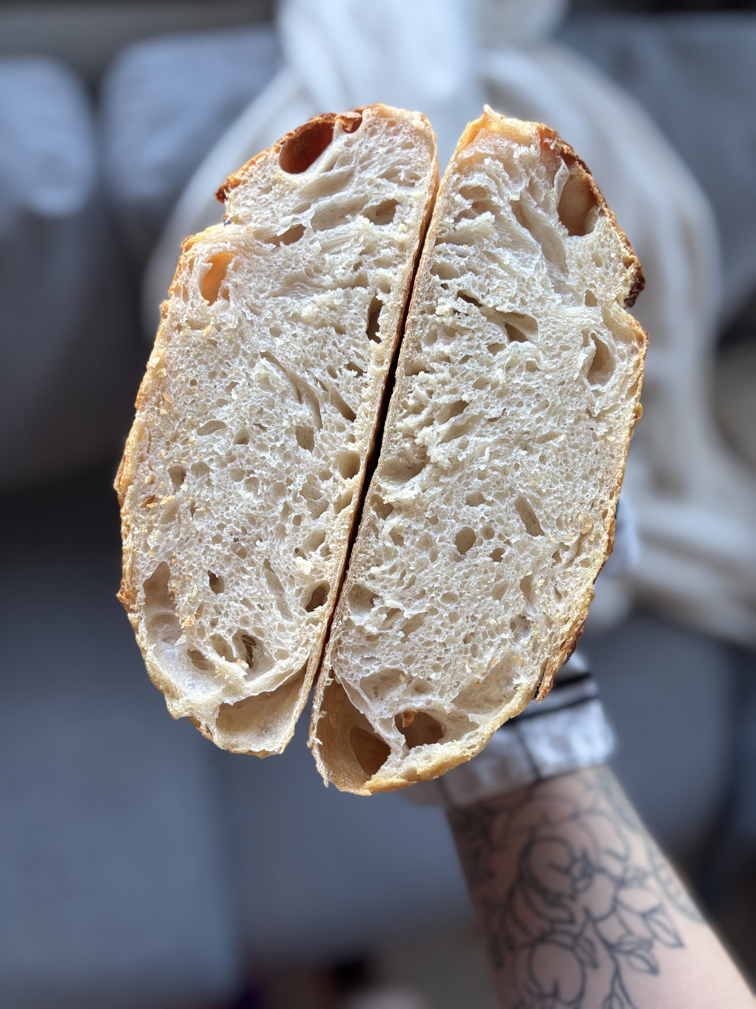 Et stykke med baguette som er delt i to, med en brukende hånd som har en tatovering på underarmen. Bakgrunnen er uklar.