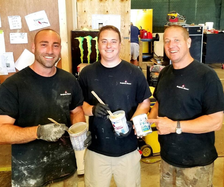 Three men painting with plaster, smiling, indoors with tools and supplies in the background.