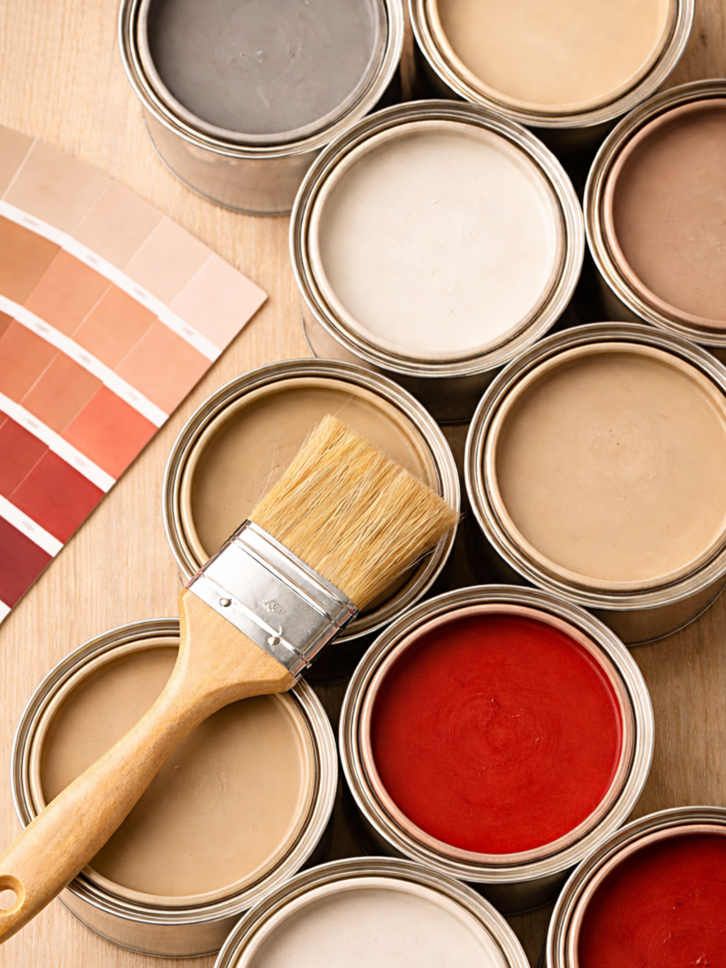 Open cans of paint in various colors on a wooden surface, with a paintbrush resting on one of the cans.