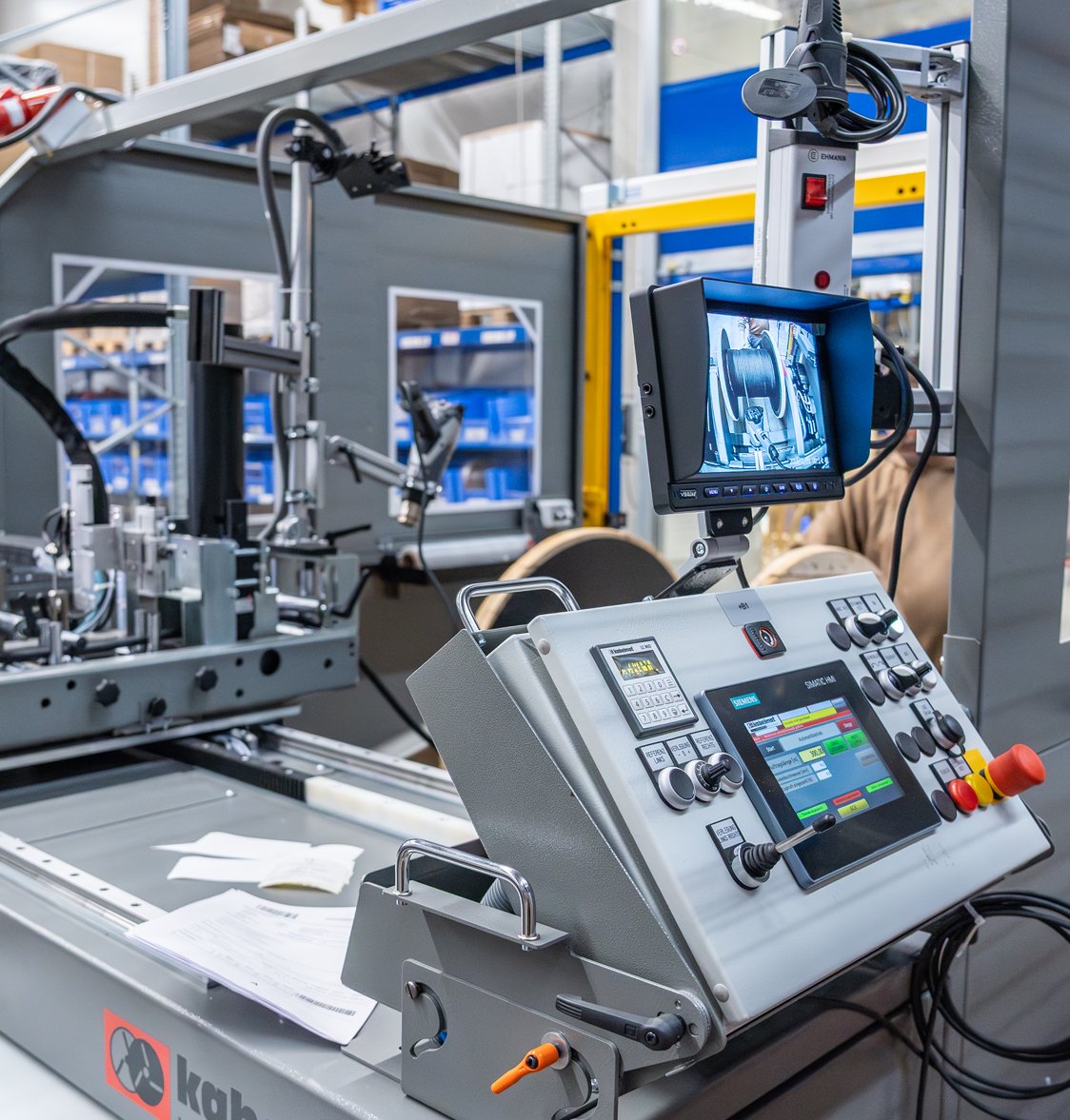 Eine Steuerungseinheit in einer Fabrikhalle, mit mehreren Bildschirmen und technischen Komponenten für die Maschinensteuerung.