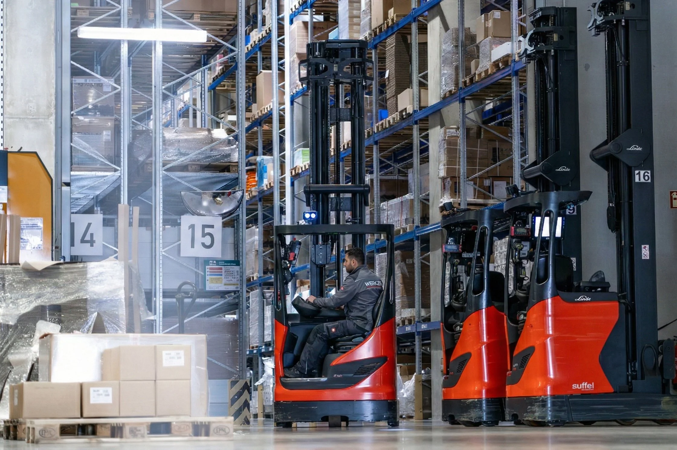 Mitarbeiter in einem Lager arbeiten mit Gabelstaplern, die Regale mit Kartons und Paketen füllen.