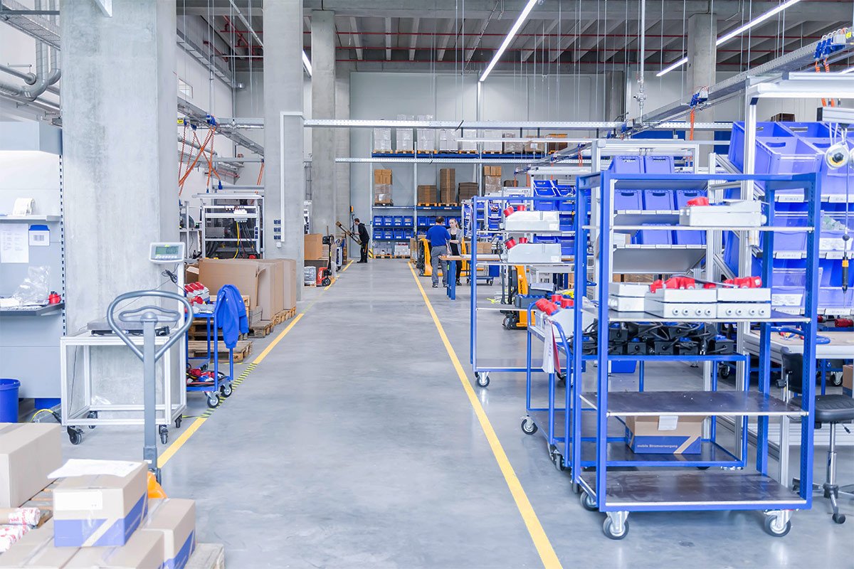 Innenansicht eines Lagerhauses mit Regalen, Kisten und Mitarbeitern bei der Arbeit.