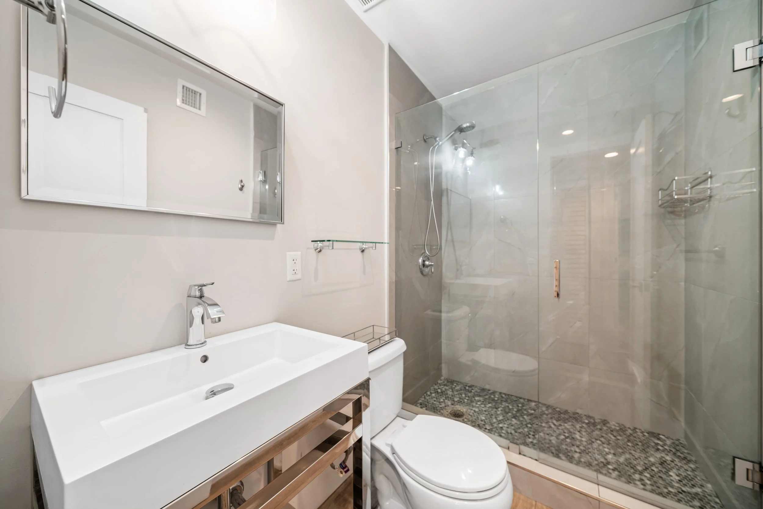 Modern bathroom with a white sink, a toilet, a large mirror, and a walk-in shower with glass doors and tiled walls.