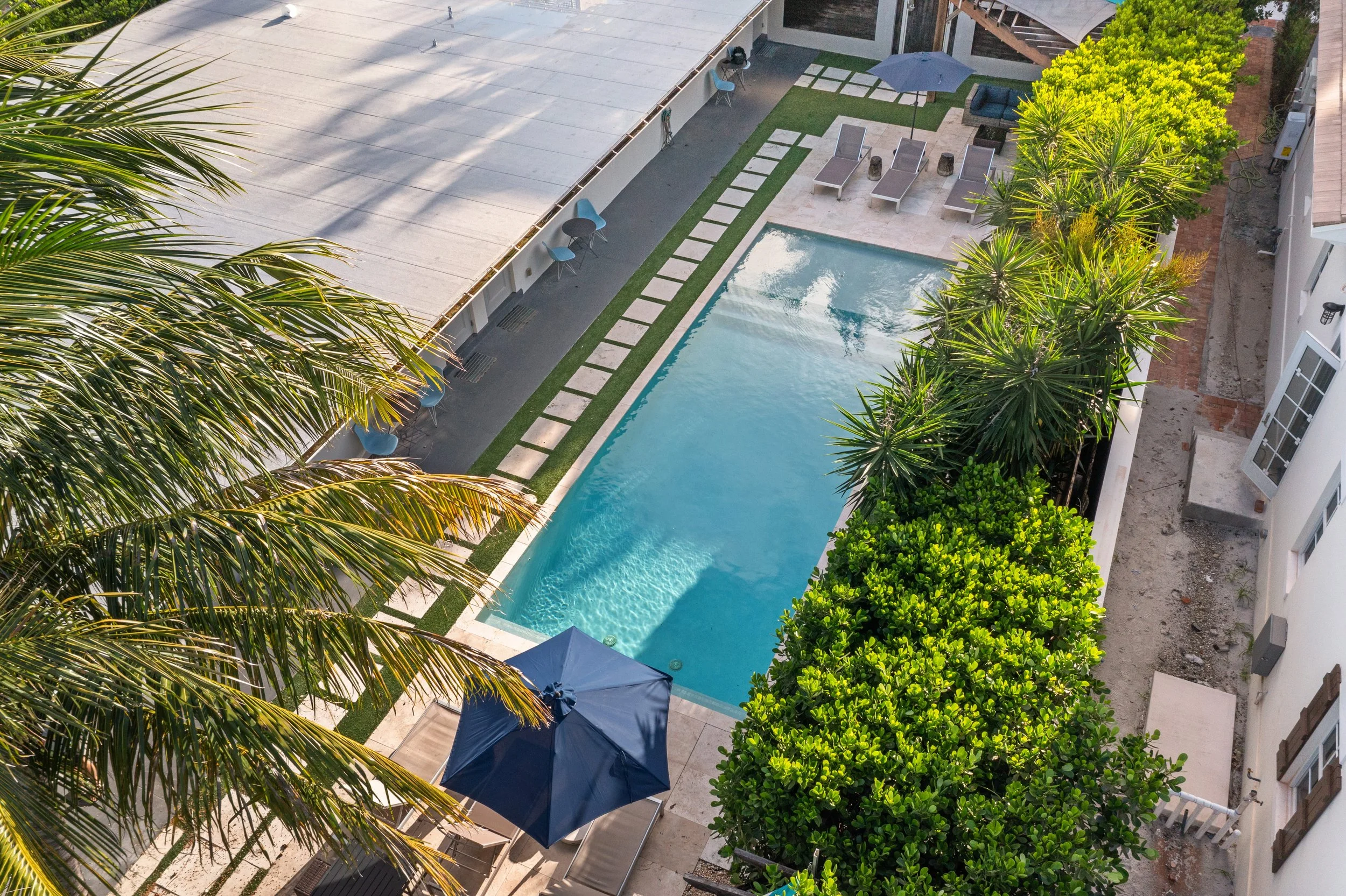 Aerial view of a backyard swimming pool with surrounding lounge chairs, umbrellas, and lush green trees.