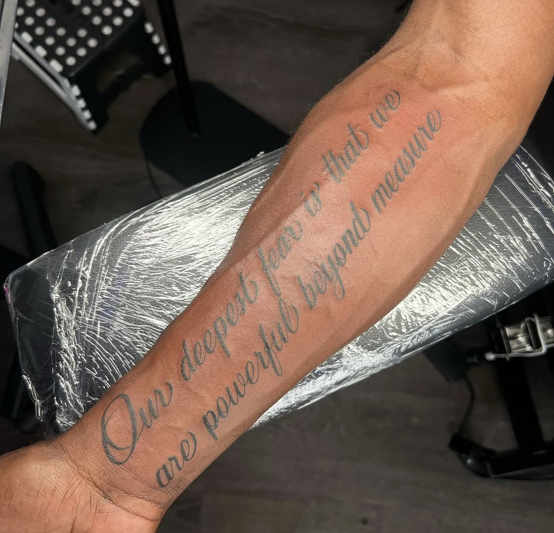 A person's forearm with a tattoo that reads, "Our desire for that we are powerless beyond measure," in cursive.