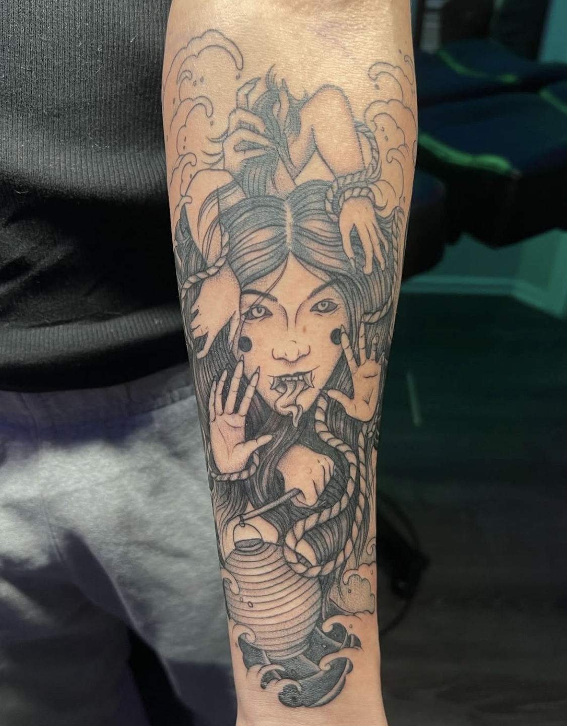 Tattoo of a mythological creature resembling Medusa with hair made of snakes, with a woman's face, pointed ears, and snake tongue, surrounded by clouds and water waves.