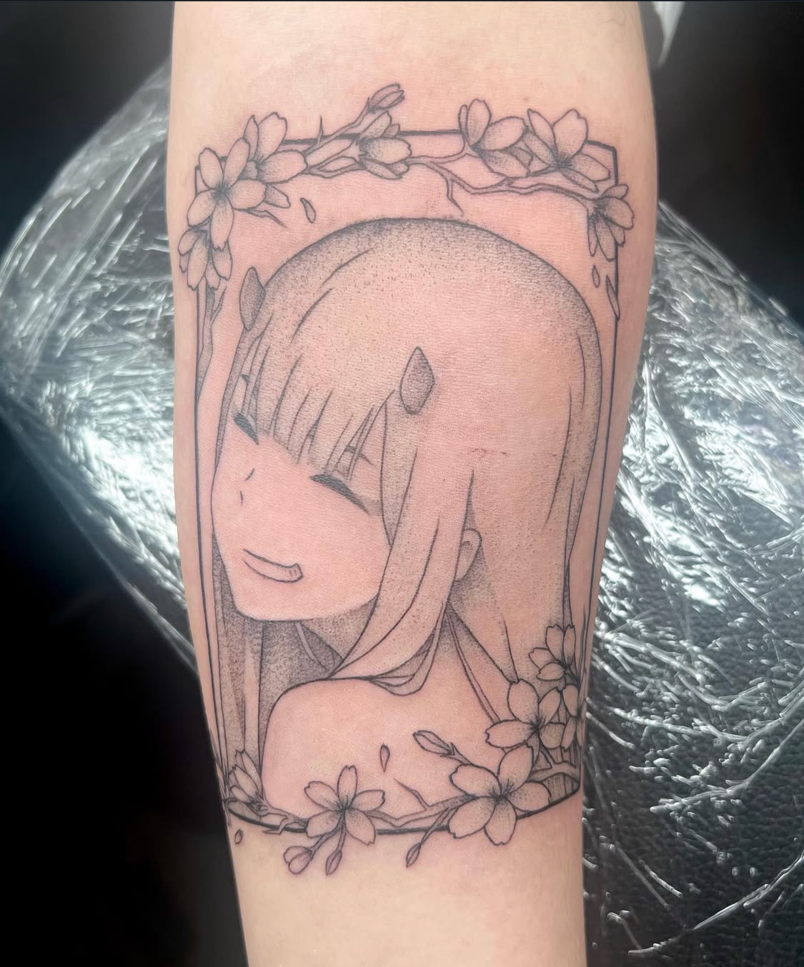 Tattoo of a smiling anime girl with long hair, surrounded by cherry blossoms.