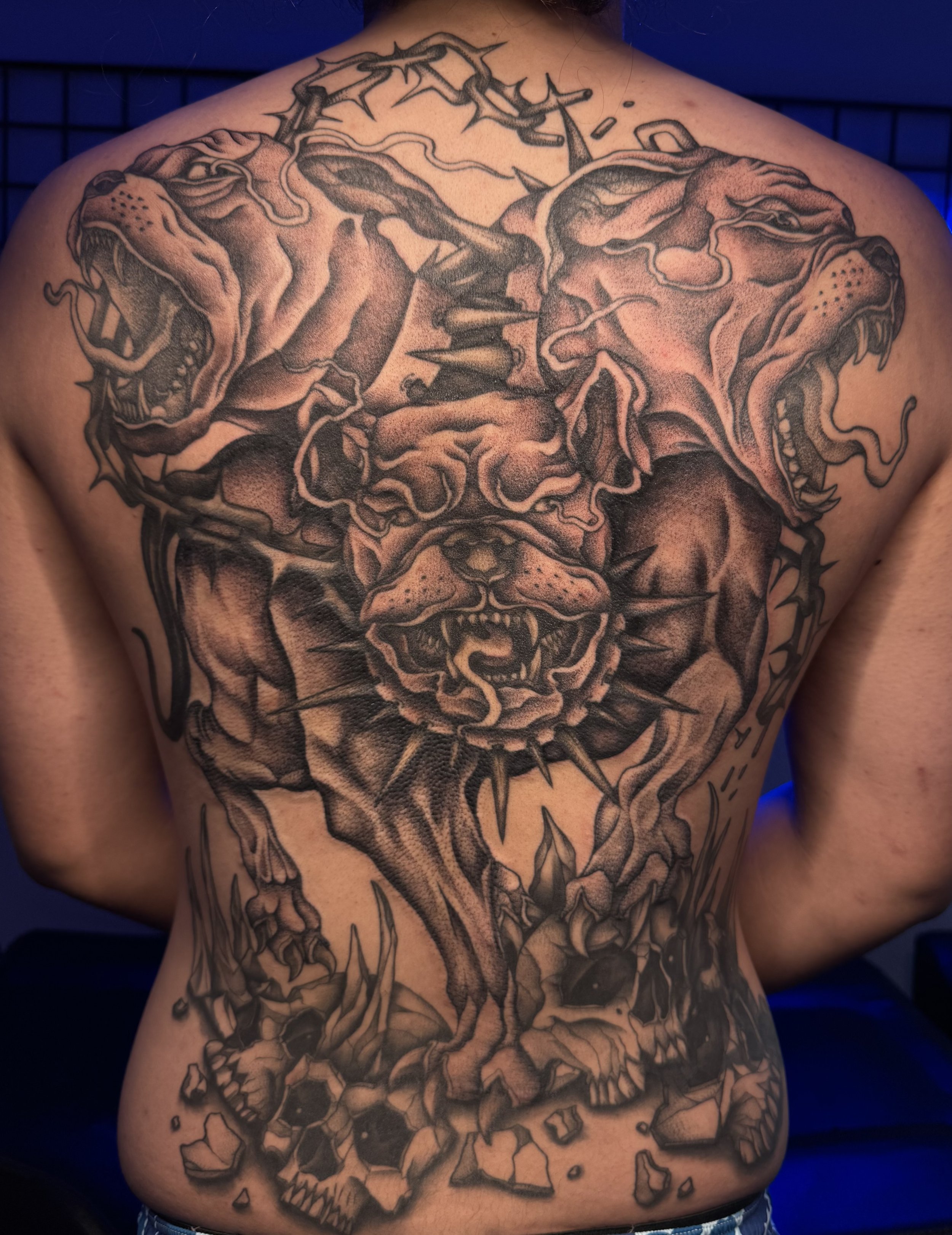 Detailed black and gray tattoo on person's back featuring a fierce lion's face, two snarling wolves, and a skull with broken stones at the bottom.