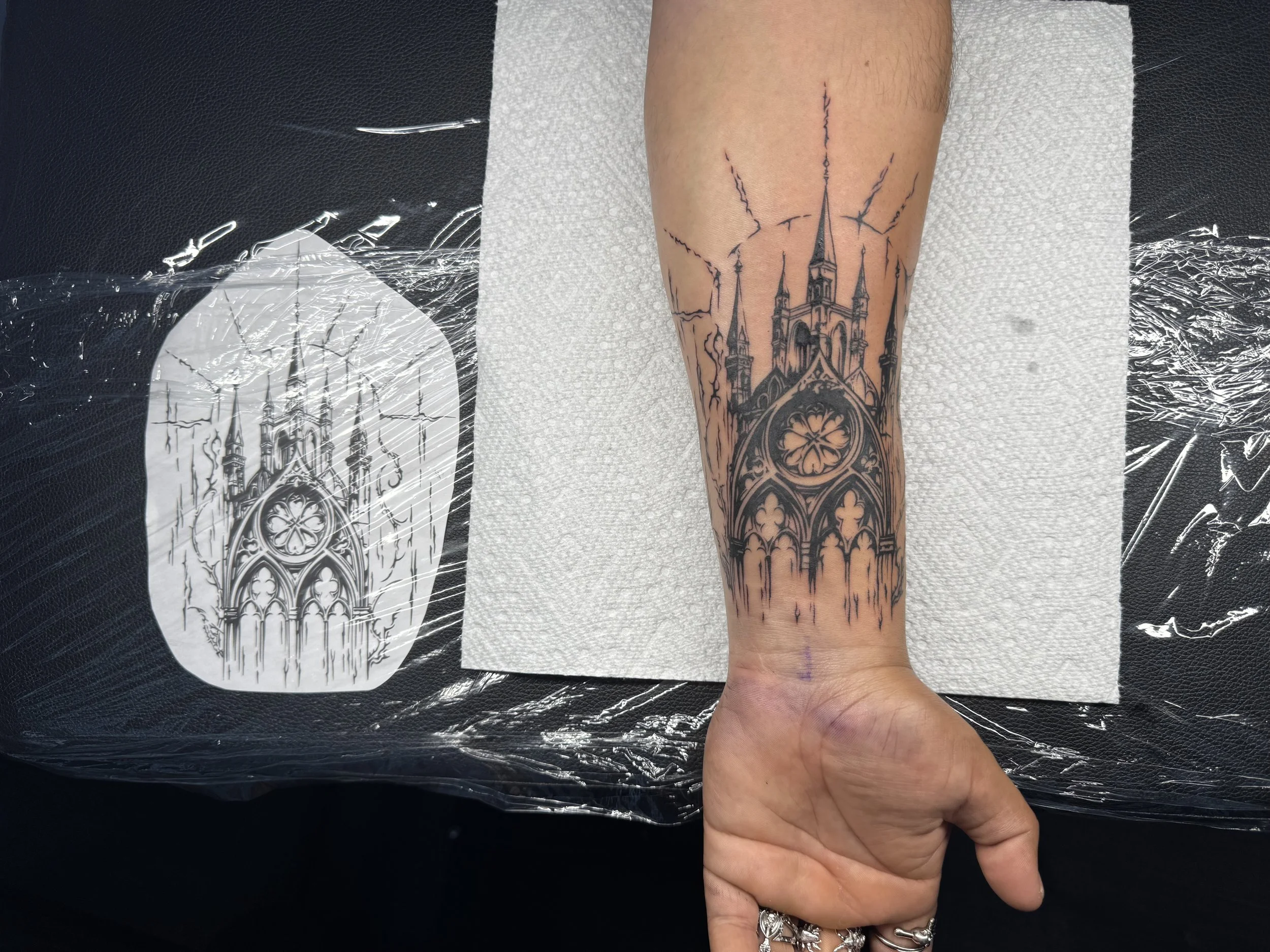 Tattoo of a Gothic cathedral on person's forearm, with detailed architecture and lightning-like lines above and around it.