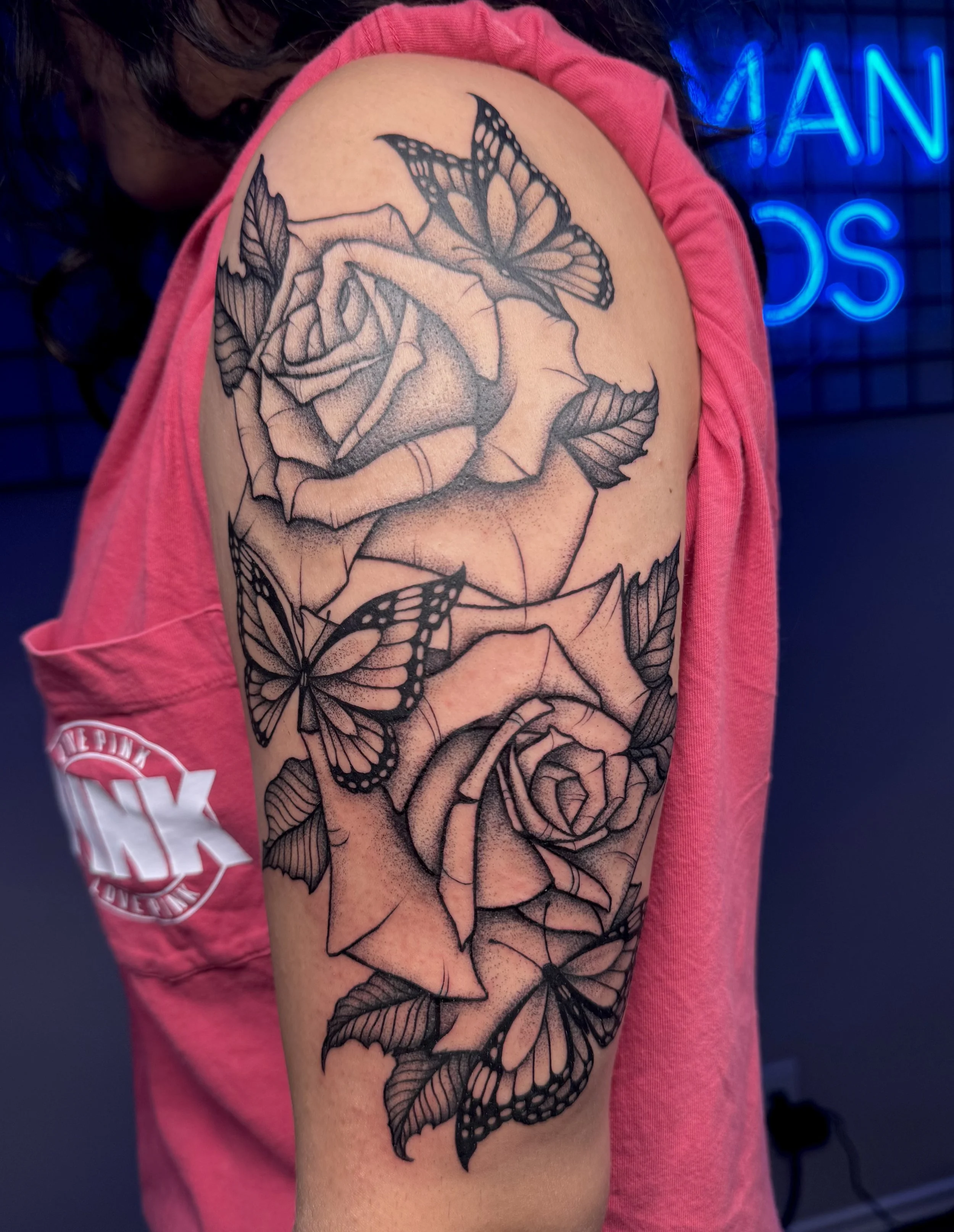 Black and gray tattoo of roses and butterflies on a person's upper arm.