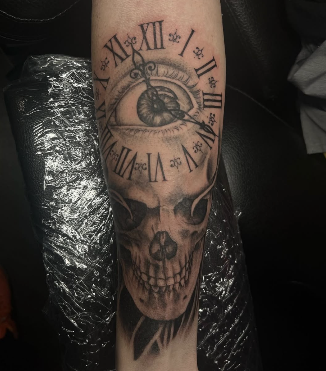 Tattoo of a skull with a clock face showing Roman numerals, an eye with detailed shading, and ornate clock hands.
