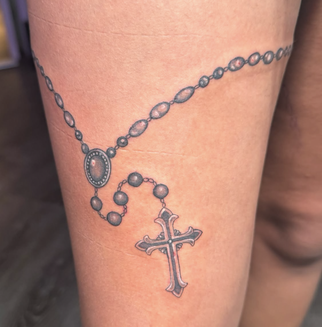 Tattoo of a rosary with a cross on a person's skin.