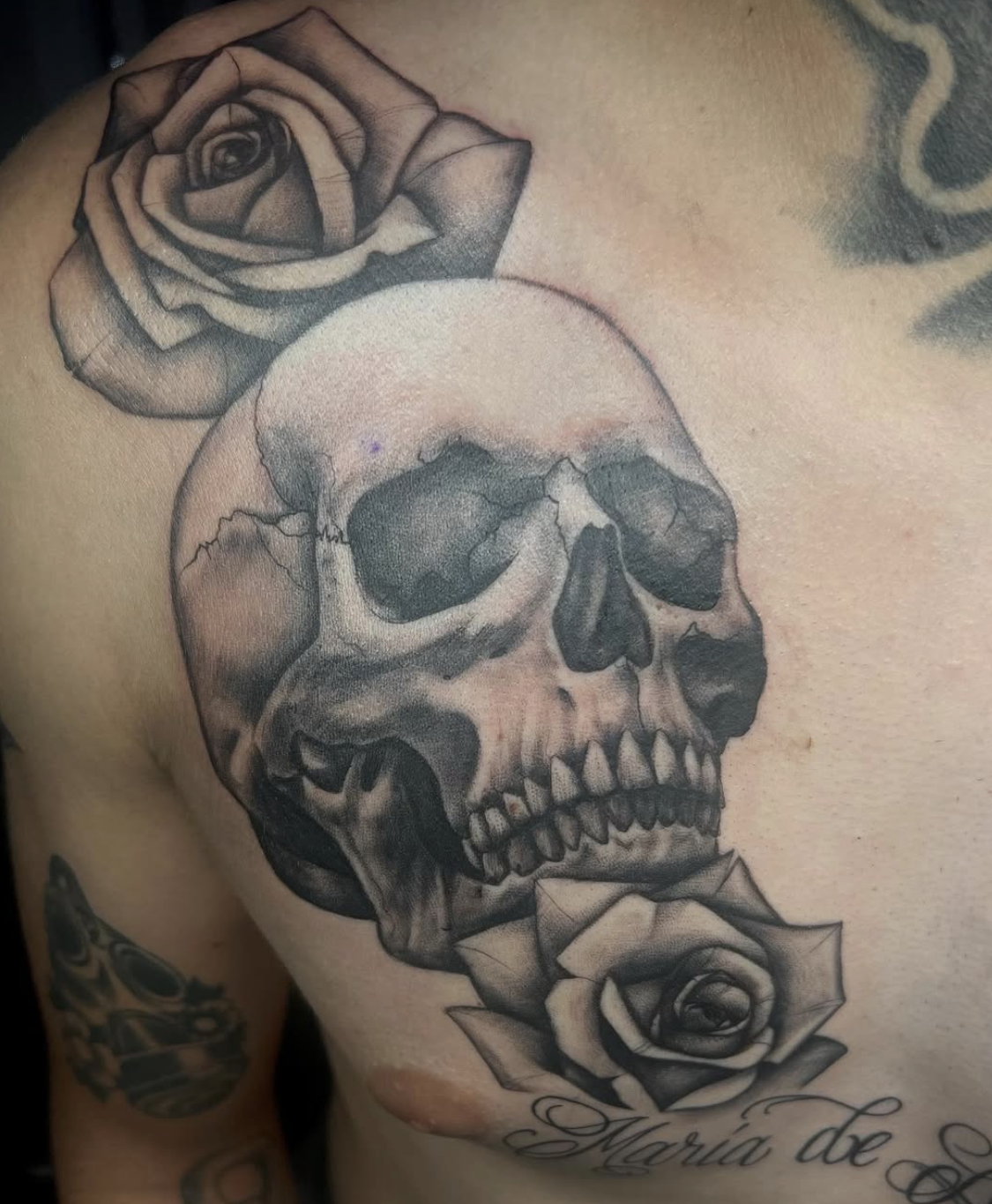 Tattoo of a skull with roses on the shoulder.