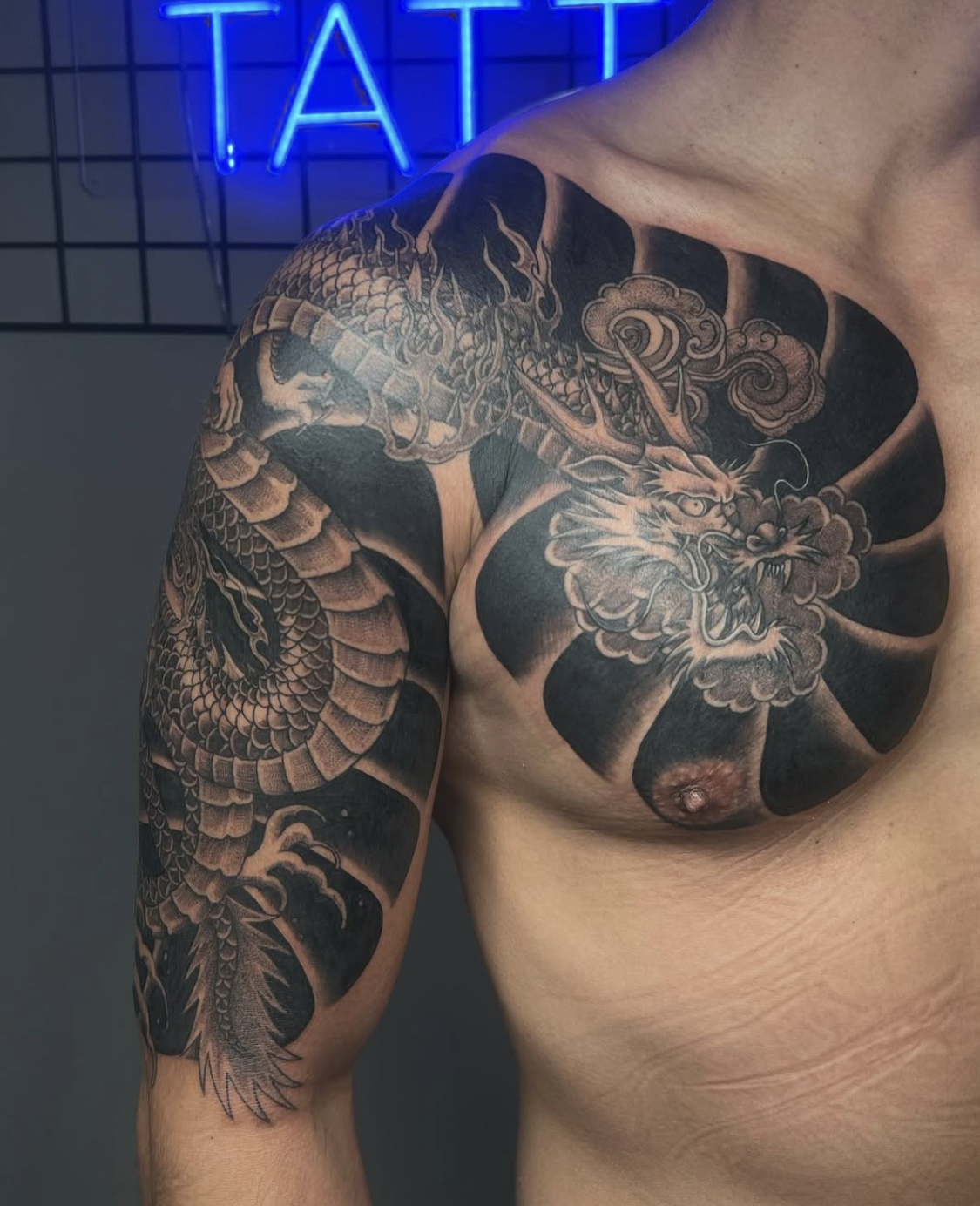 Close-up of a person's shoulder and upper arm with a detailed black and gray tattoo of a dragon and a tiger, featuring clouds and traditional Japanese style elements.
