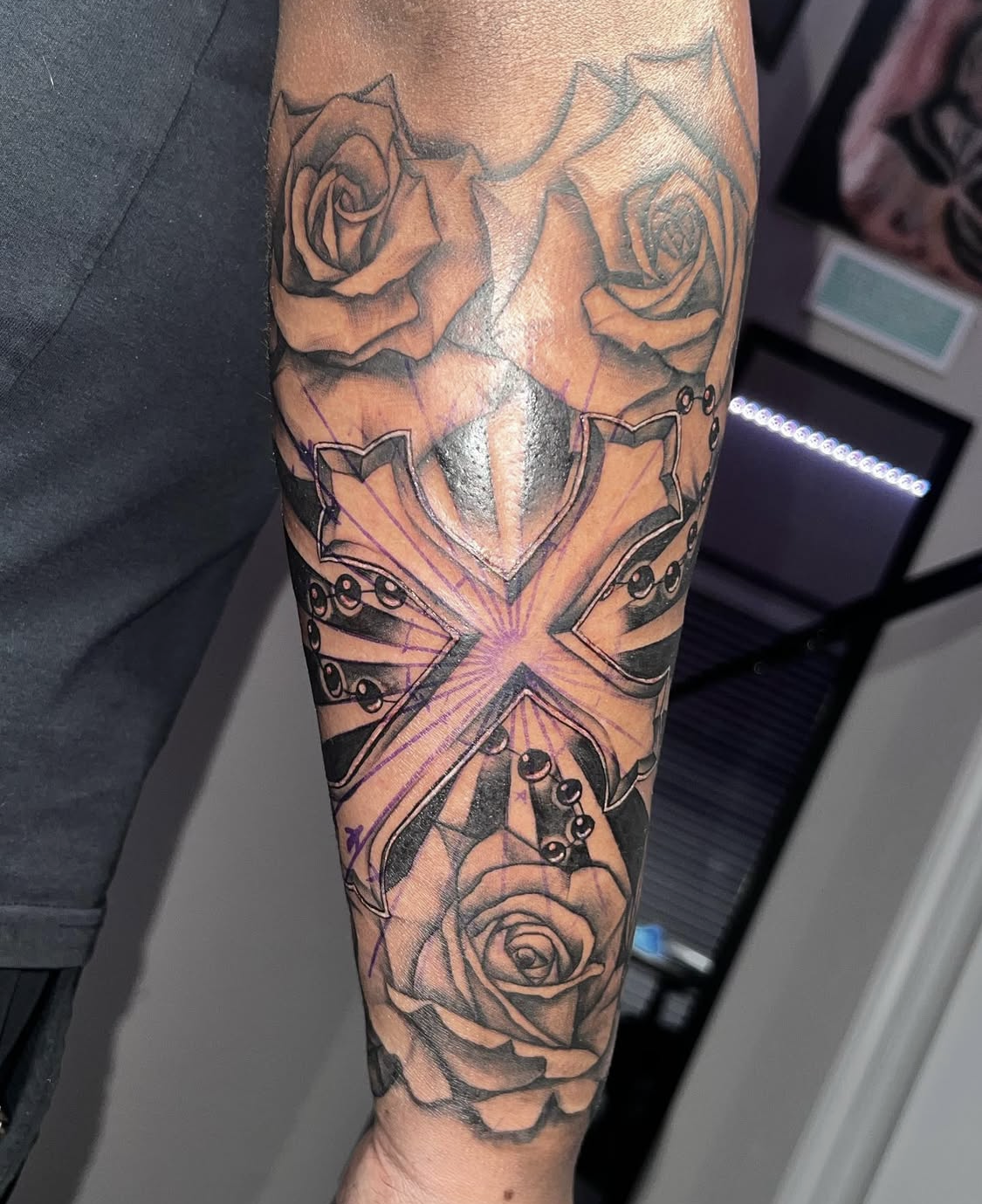 Tattoo of roses, a dagger, a cross, and a rosary on a person's arm.