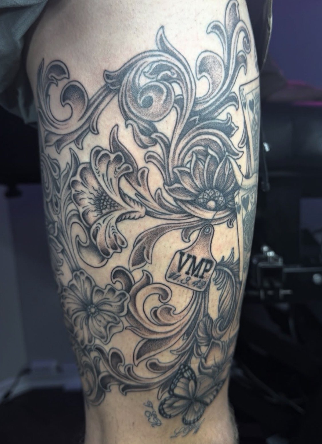 Black and gray floral tattoo with a vehicle emblem reading 'VMP' on the upper arm.