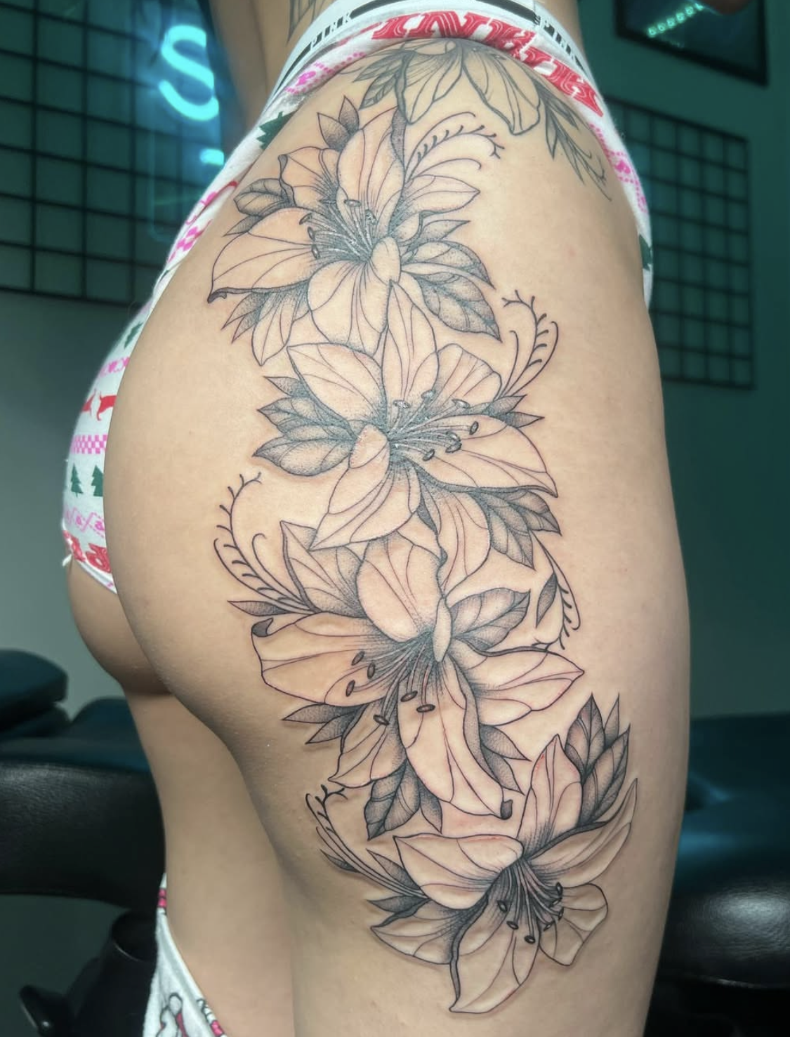 A thigh tattoo featuring intricate line art of lilies and butterflies.