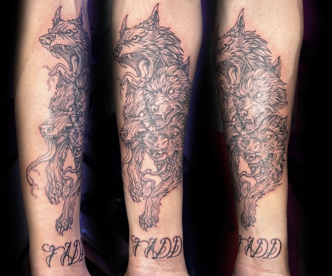 Tattoo of three wolves in different poses, outlined in black on a person’s forearm, with the initials 'WDD' in cursive below.