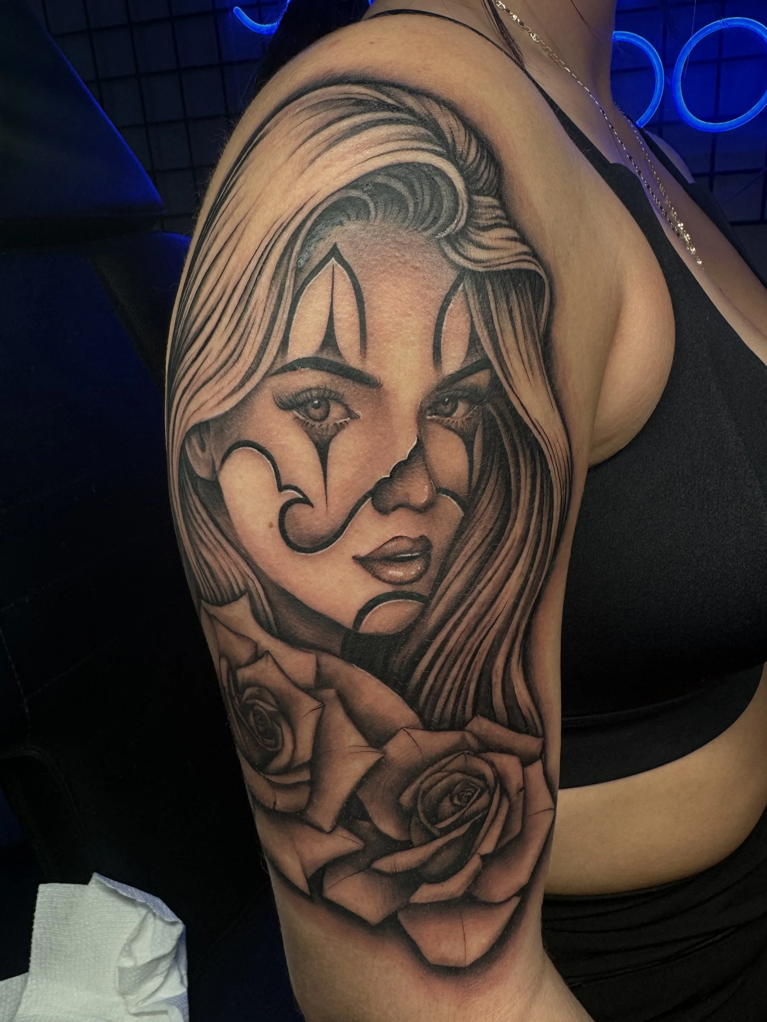Black and gray tattoo of a woman's face with long flowing hair and roses on her shoulder.