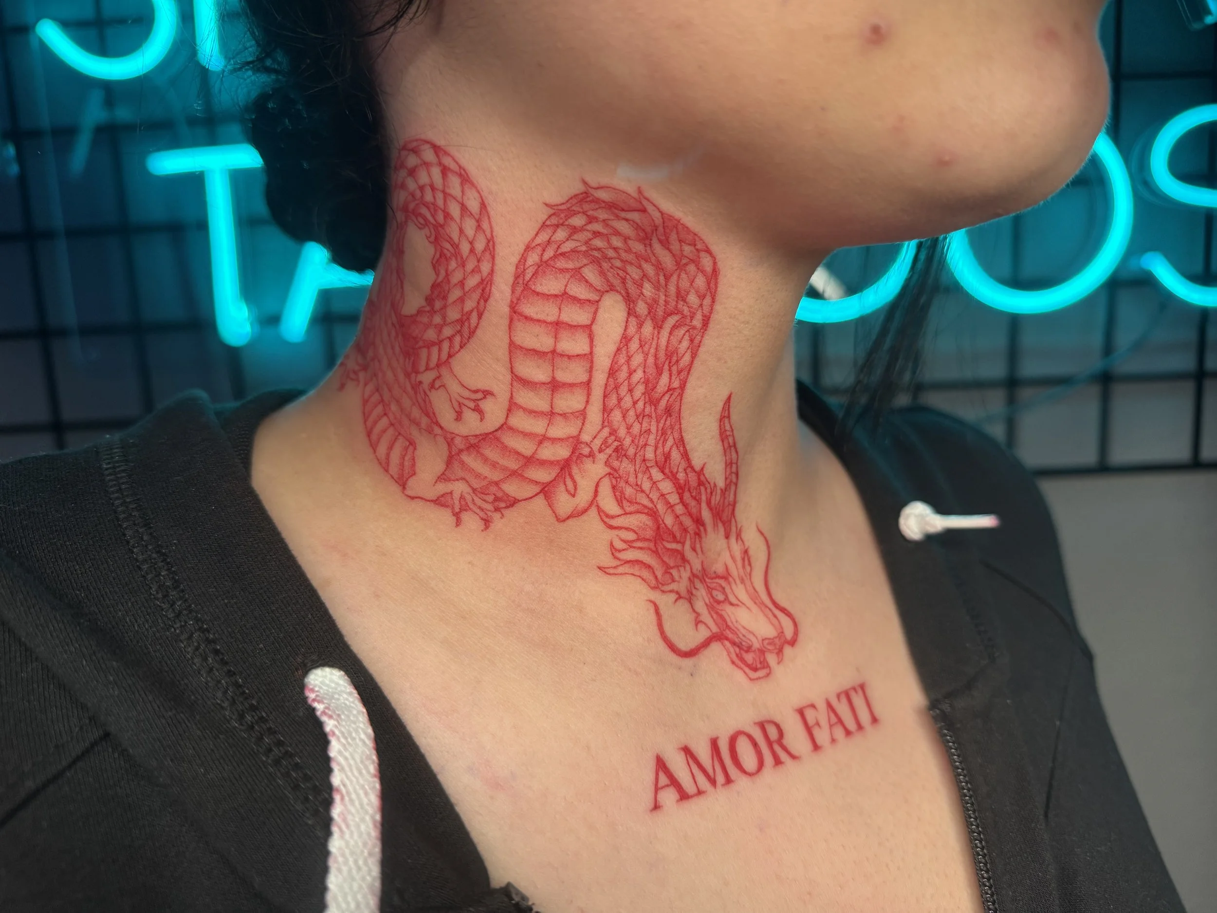 Red tattoo of a dragon's head and body on a person's neck, with the words "AMOR FATI" below.