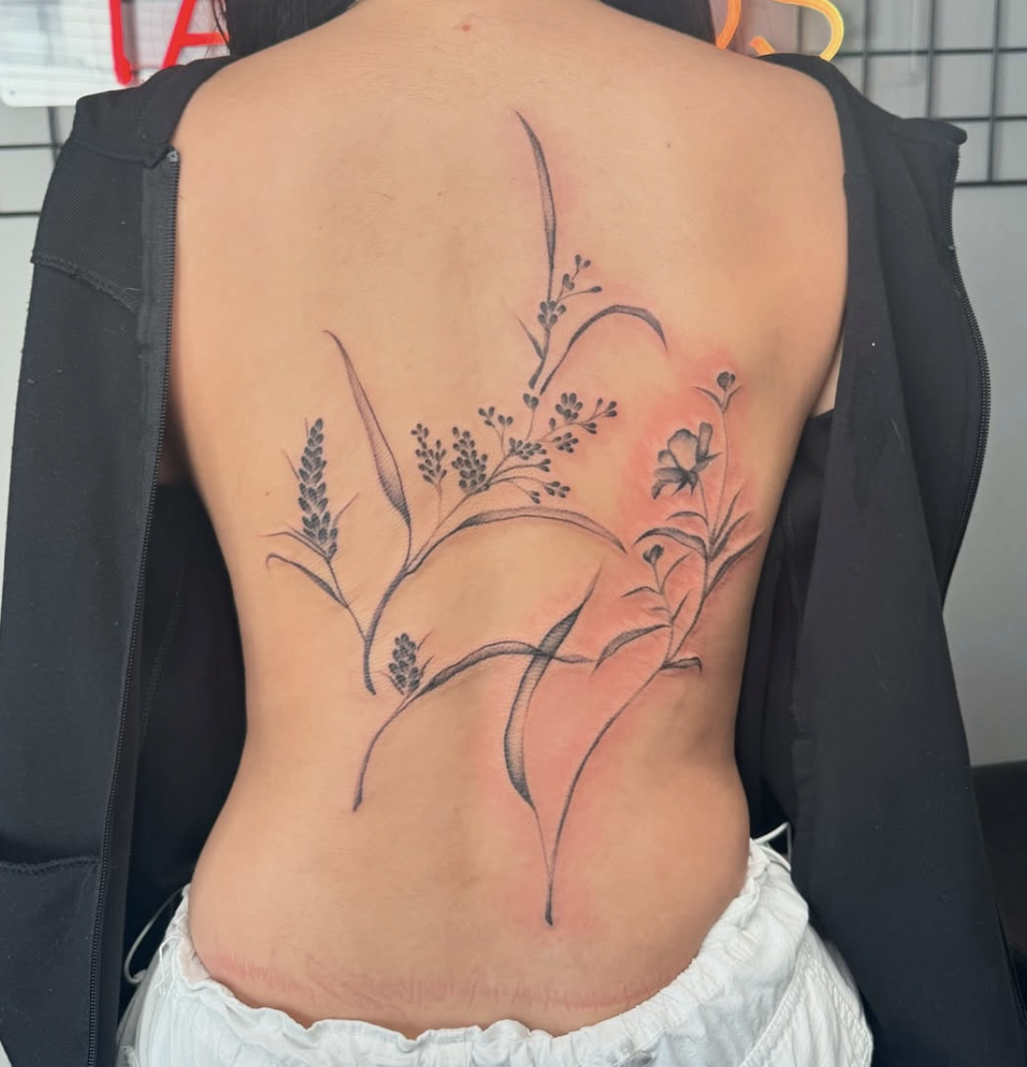 Tattoo of black floral and grass patterns on a person's side and back.