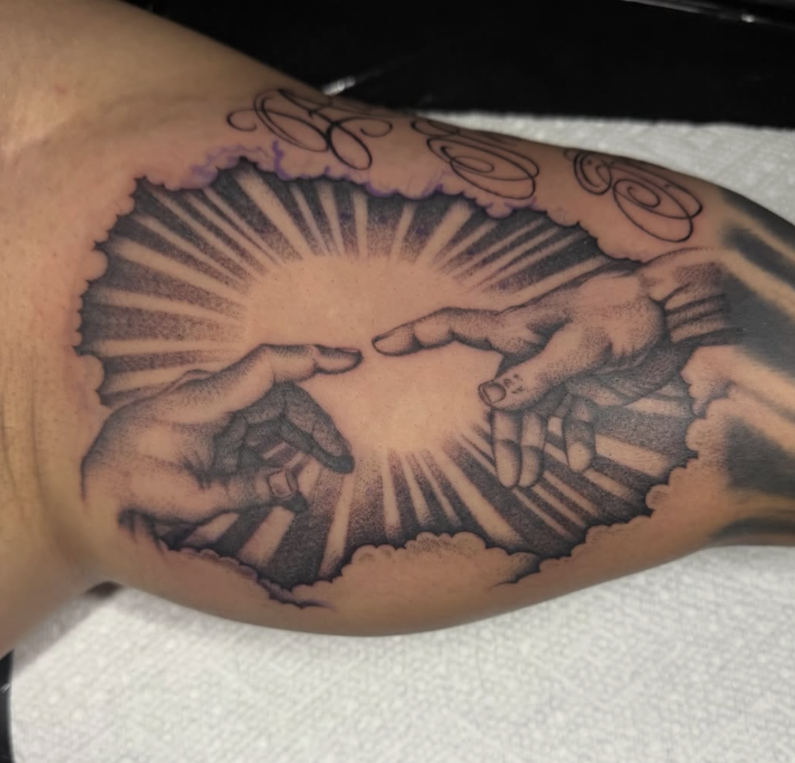 Tattoo of two hands reaching towards each other, surrounded by clouds and rays of light.