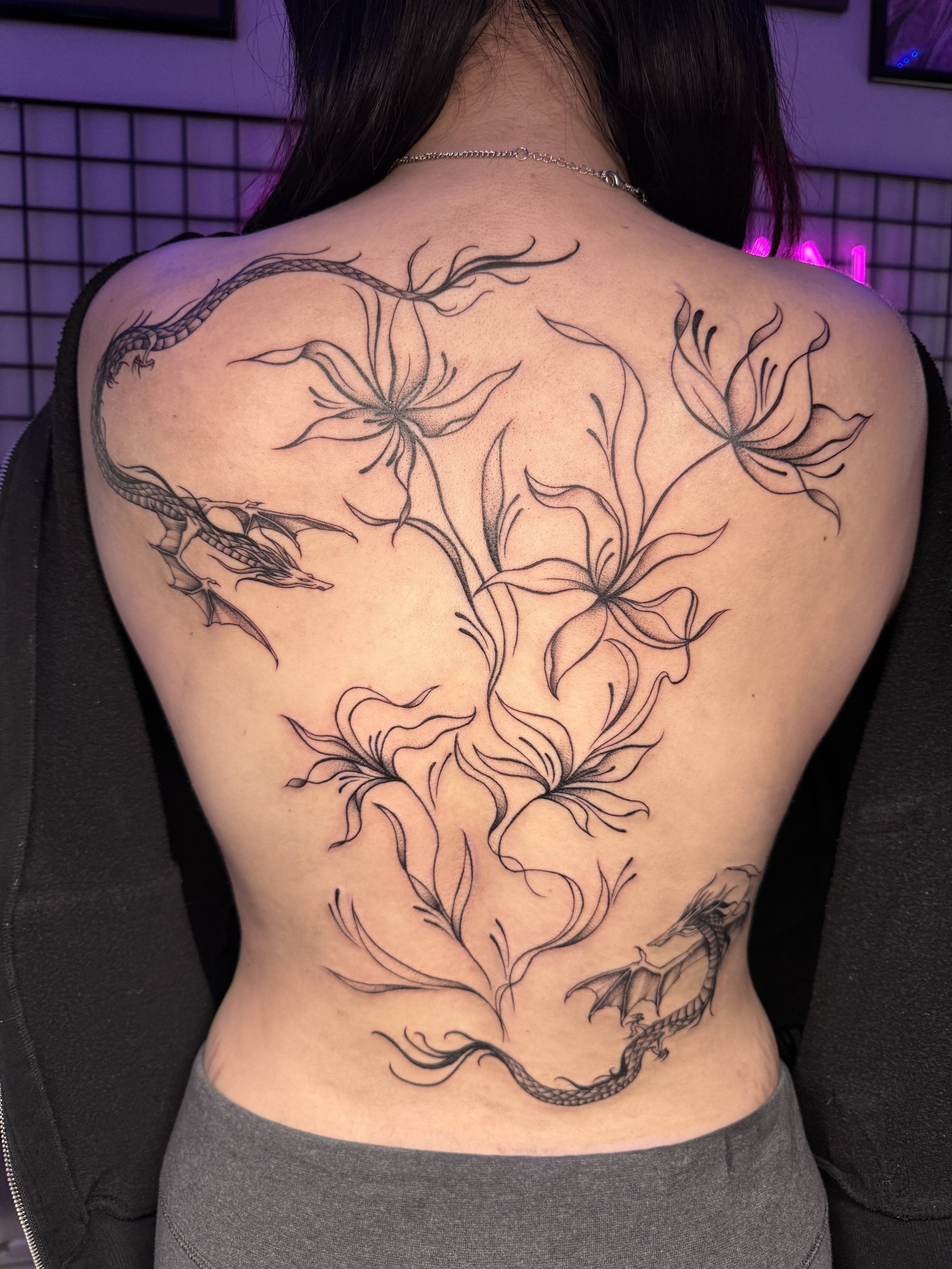Black outline dragon tattoo with floral design on person's back.